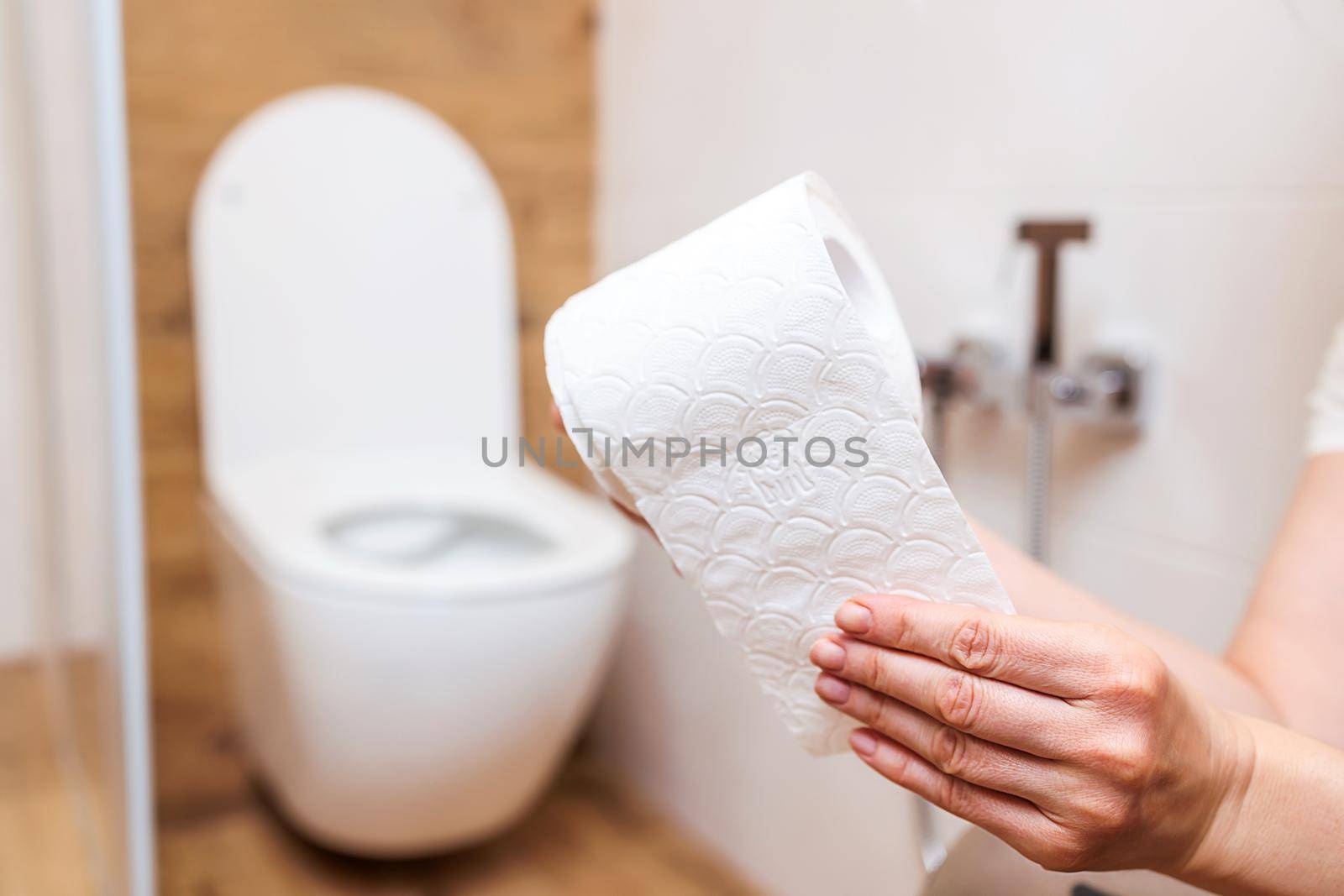 close-up, woman's hand tears off sheet from roll of toilet paper on the background of bathroom. The concept of health problems, treatment of hemorrhoids, intestines. Personal hygiene and health care