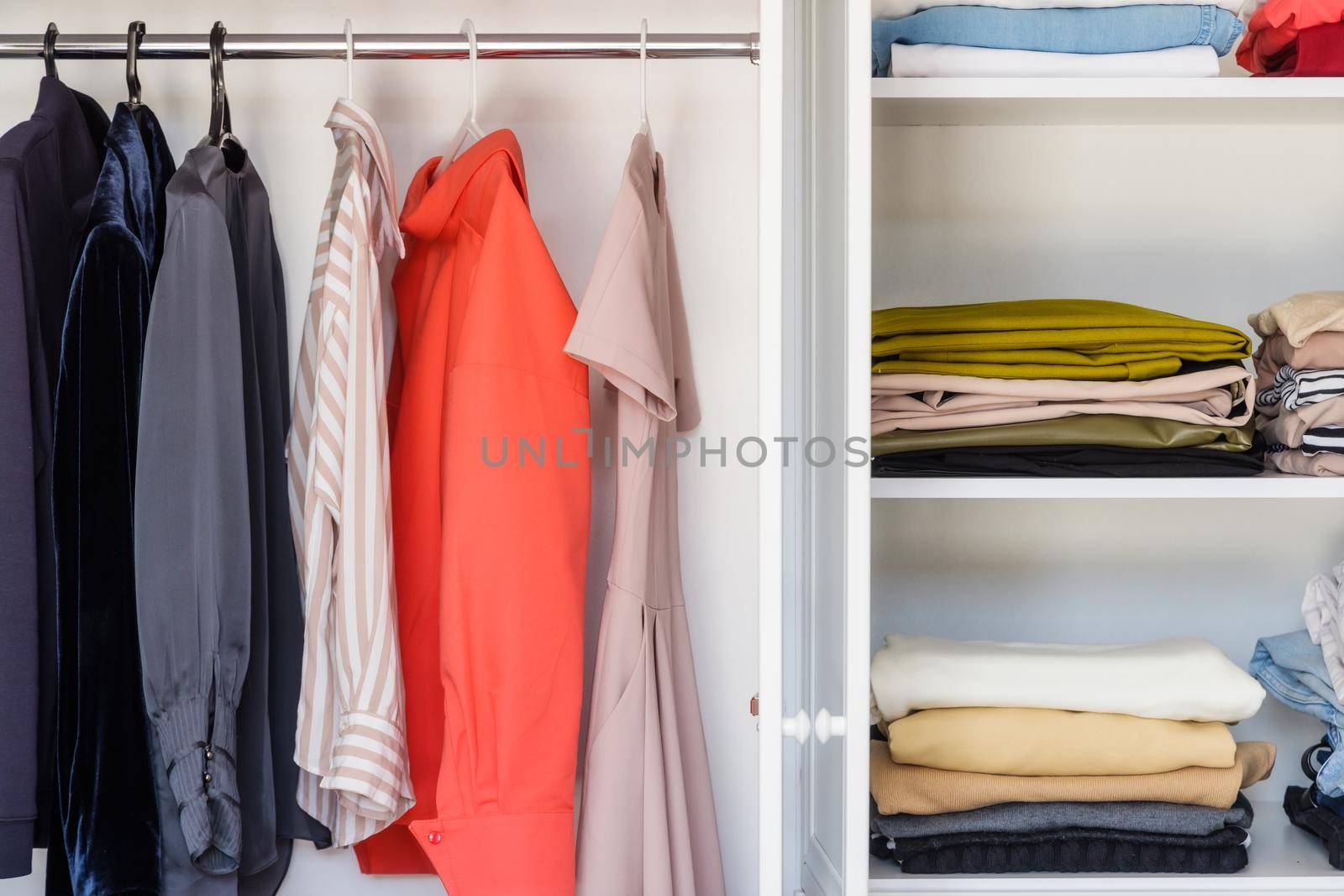 Shelves with colorful clothes in a white wardrobe close-up, minimalism style by Ramanouskaya