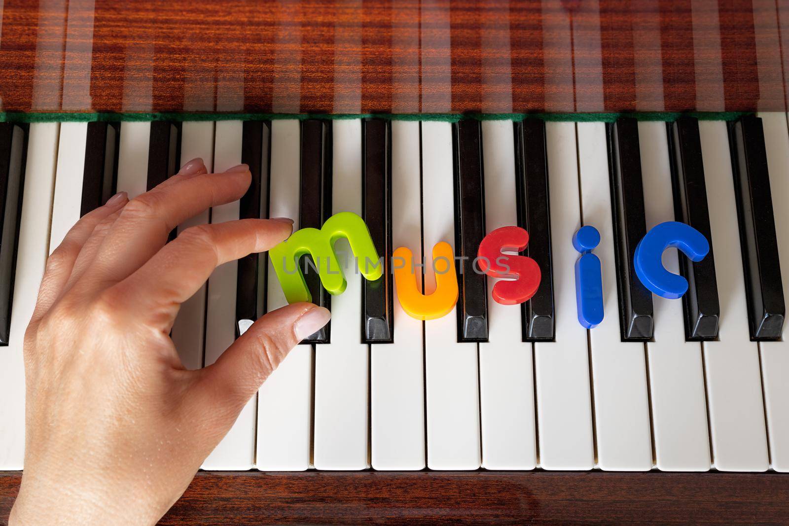 Female hand lays out the word music from colored letters on the piano by Ramanouskaya