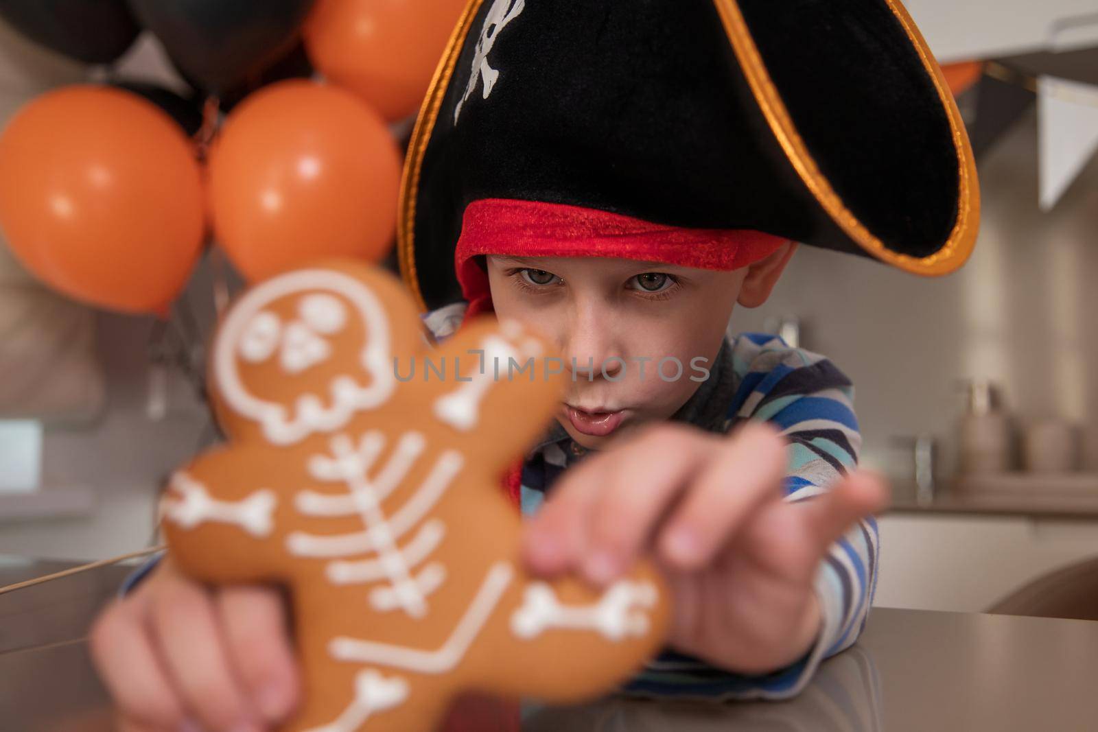 Close-up portrait of a boy dressed as a pirate for Halloween. The child eats homemade gingerbread in the form of a skeleton and shows a cookie close-up. House party concept for the whole family
