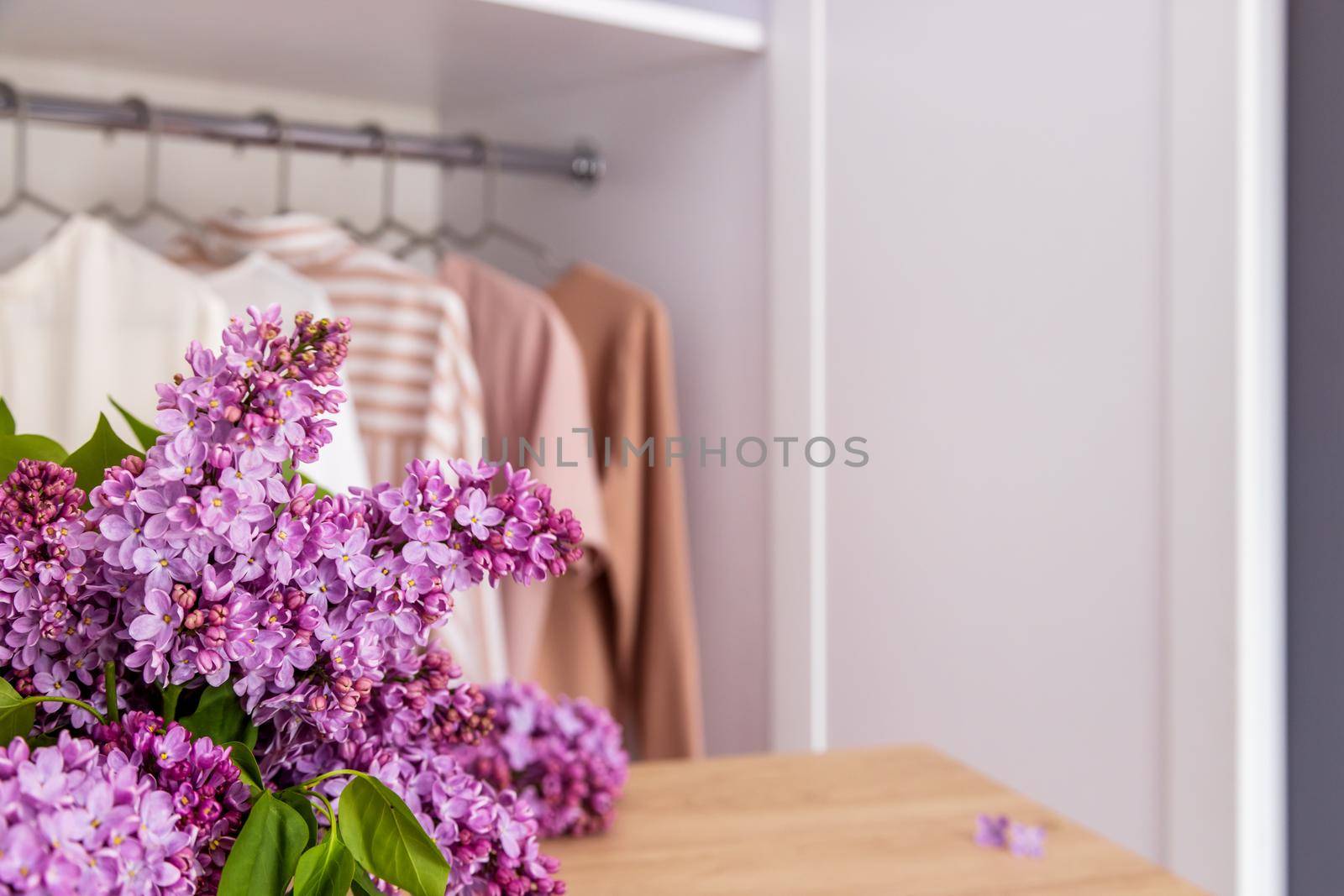 Stylist fashion wardrobe in neutral beige tones. Mockup for washing powder or bleach. Copy and paste space for text or your product. In foreground a wooden table and a branch of lilac, for the product