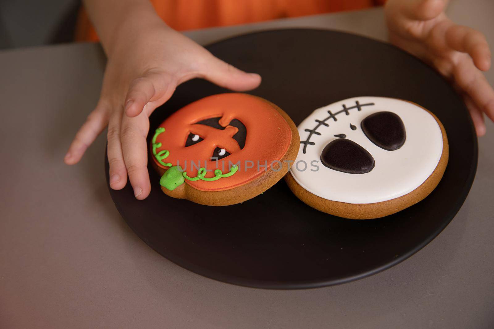 Girl's hand reaches for homemade Halloween cookies with painted faces by Ramanouskaya