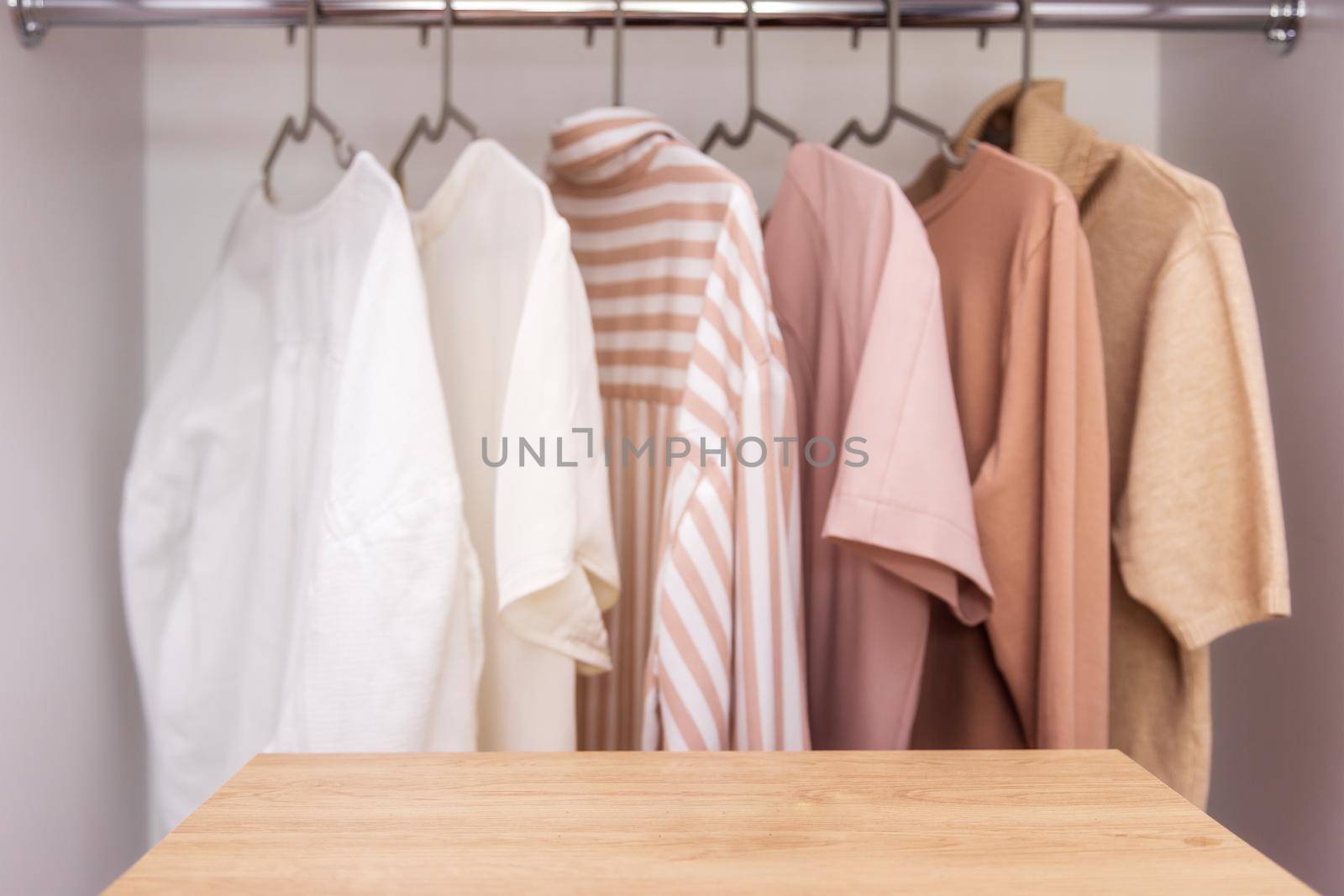 Stylist fashion wardrobe in neutral beige tones. Mockup for washing powder or bleach. Copy and paste space for text or your product. In the foreground is an empty, wooden table for product placement.