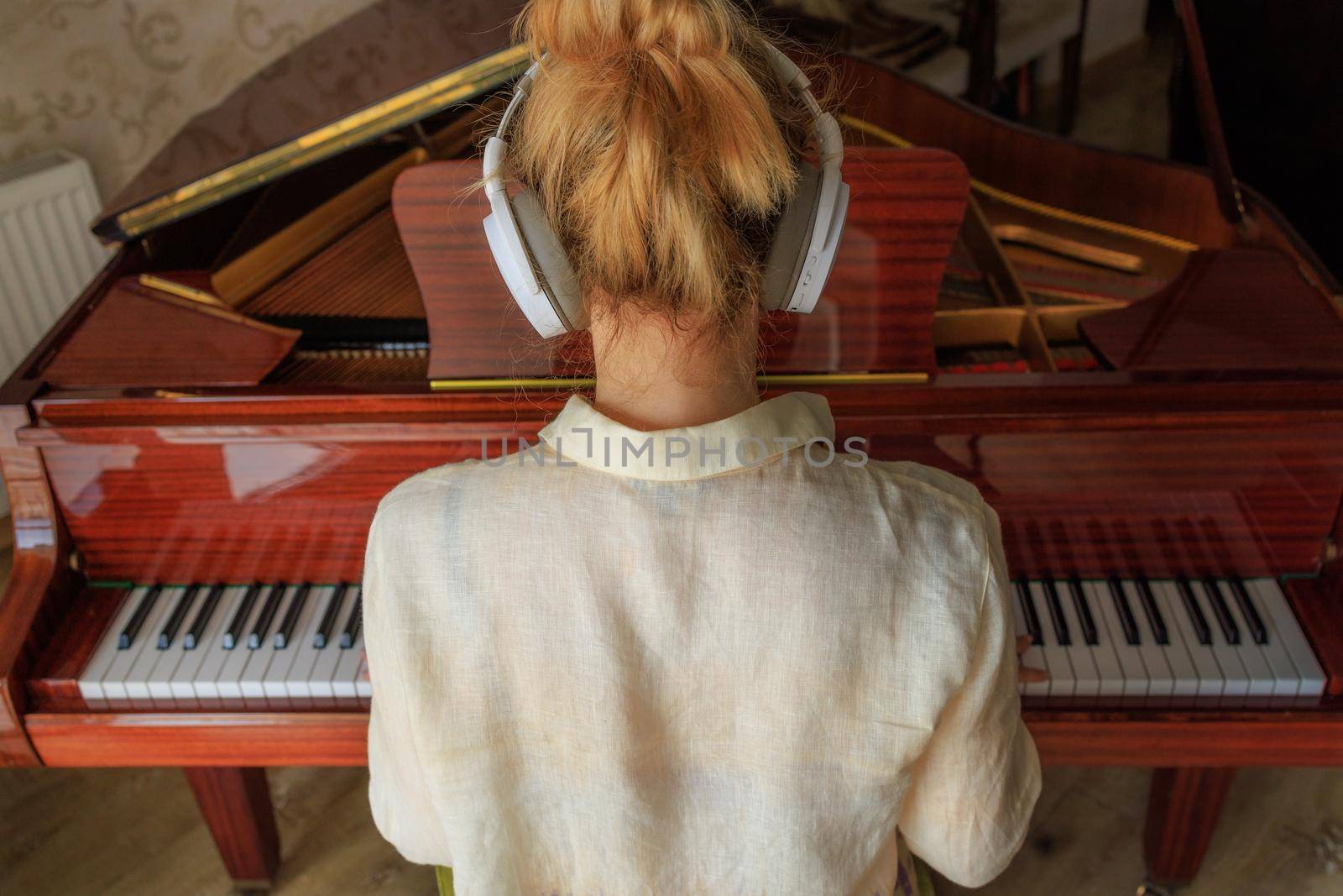 young blonde plays the retro piano. Listens to music on headphones and repeats on the piano. Lifestyle, modern approach to the study of music. Music learning concept, modern technology, music festival