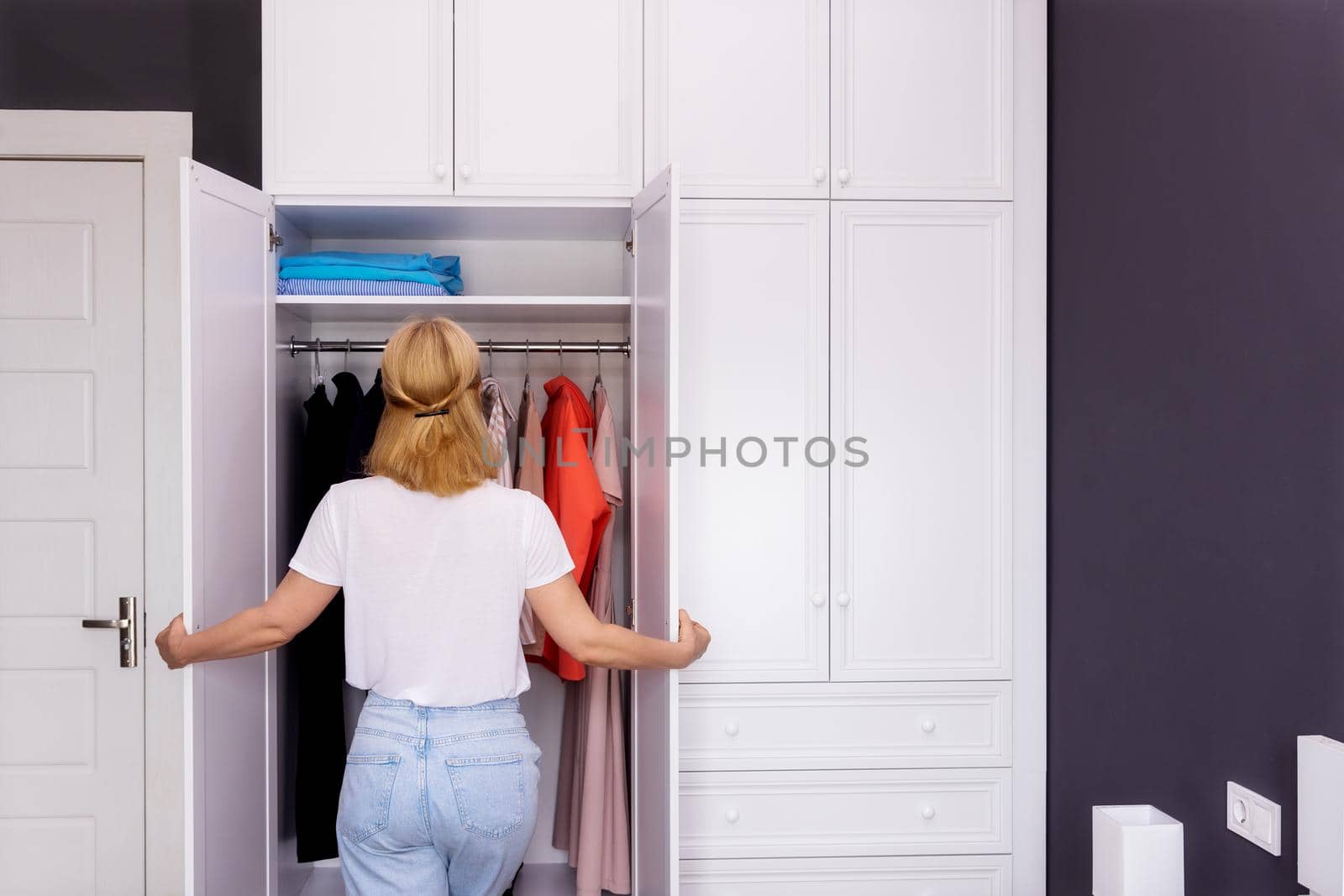A woman stands in front of a closet and chooses her clothes for a walk. by Ramanouskaya