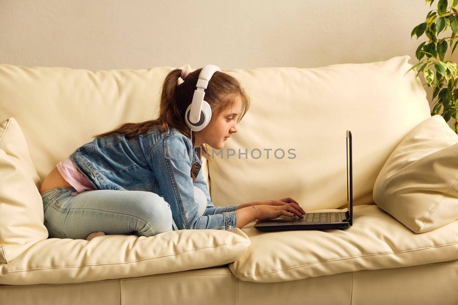 Online education. Kid girl with headphones looking video lesson teacher conference laptop sitting on the couch at home