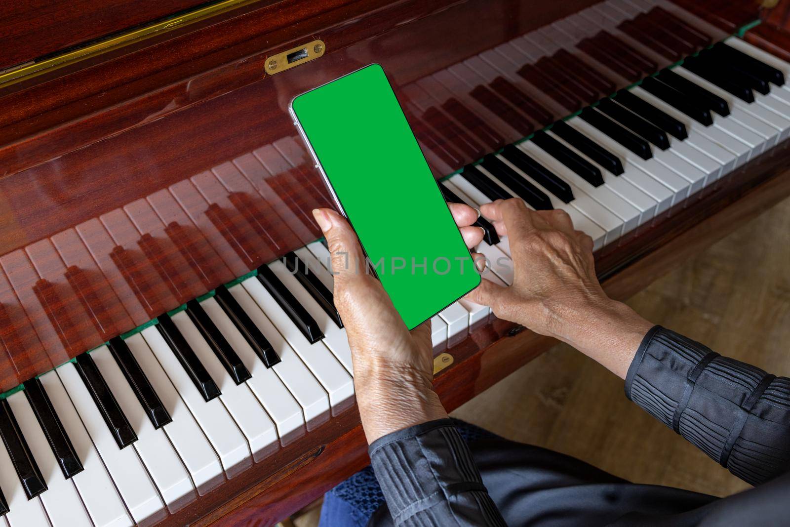 An elderly woman wants to learn how to play the piano, looks at notes on her phone. Smartphone mockup, green chroma key. template for music festival cover, learning to play a musical instrument