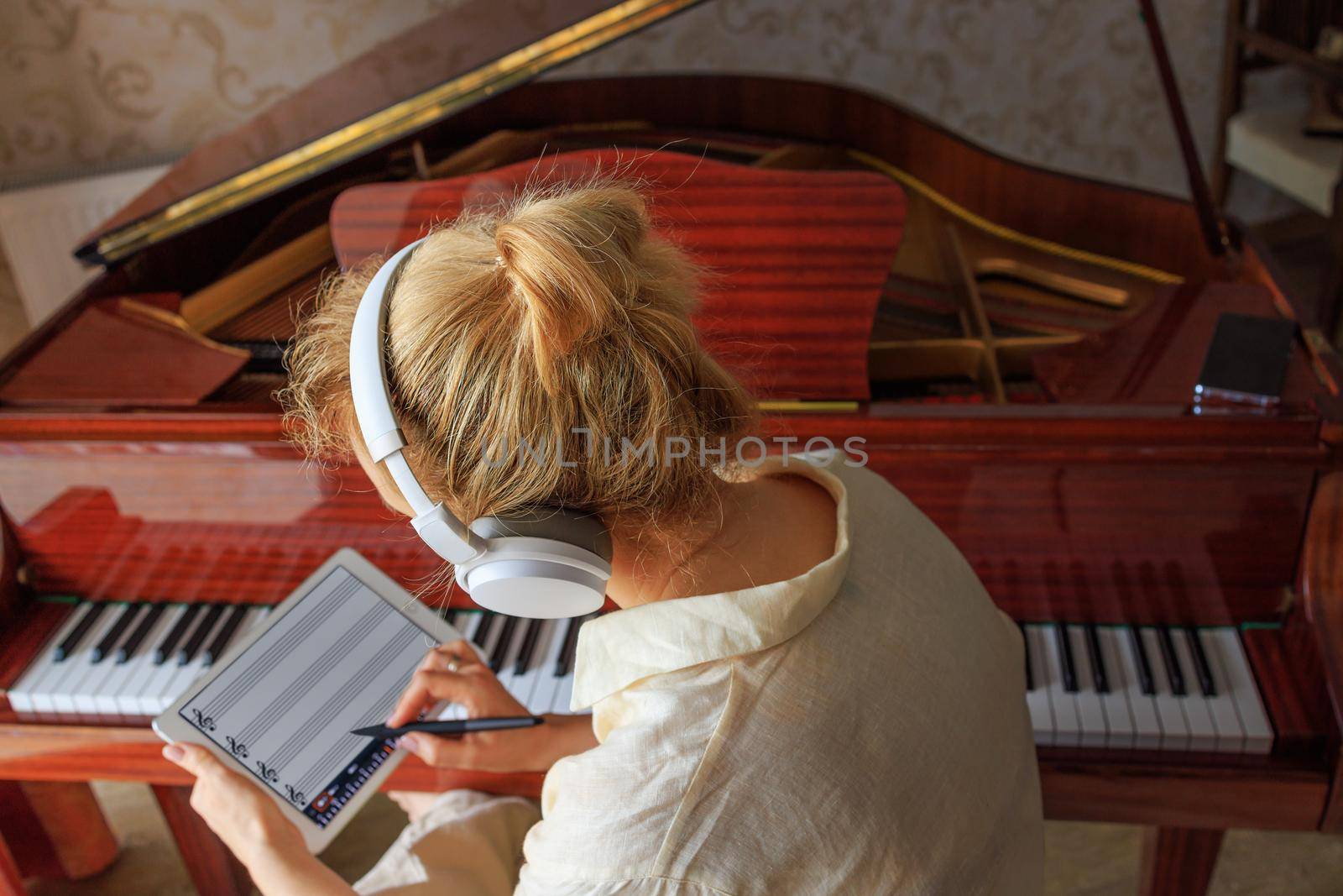 a young girl composes music near the piano and writes into the program on tablet by Ramanouskaya