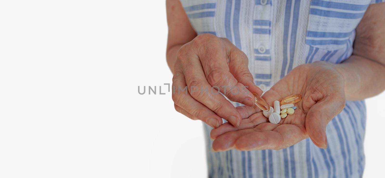 Close-up, elderly woman on a white background. In the hands of an old woman there are many different pills and vitamins for diseases. The concept of disease prevention in the elderly