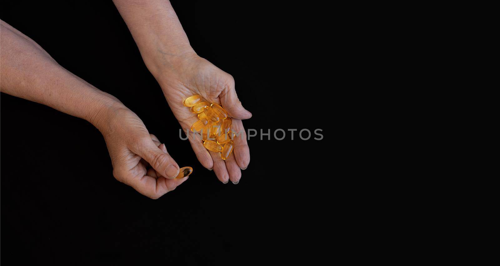 Close-up of an elderly woman's hand with a handful of Omega 3 vitamins. Black background, copy paste for your text. The concept of health prevention, taking vitamins and minerals, maintaining the body