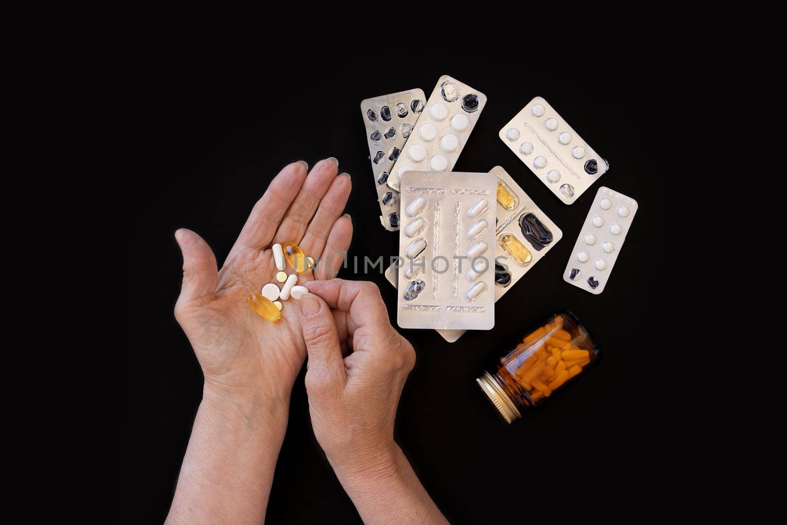 close-up, the hands of elderly woman on a black background are sorting out medicines. Lots of different pills. The concept of a large number of diseases in old age, drug treatment, age-related changes