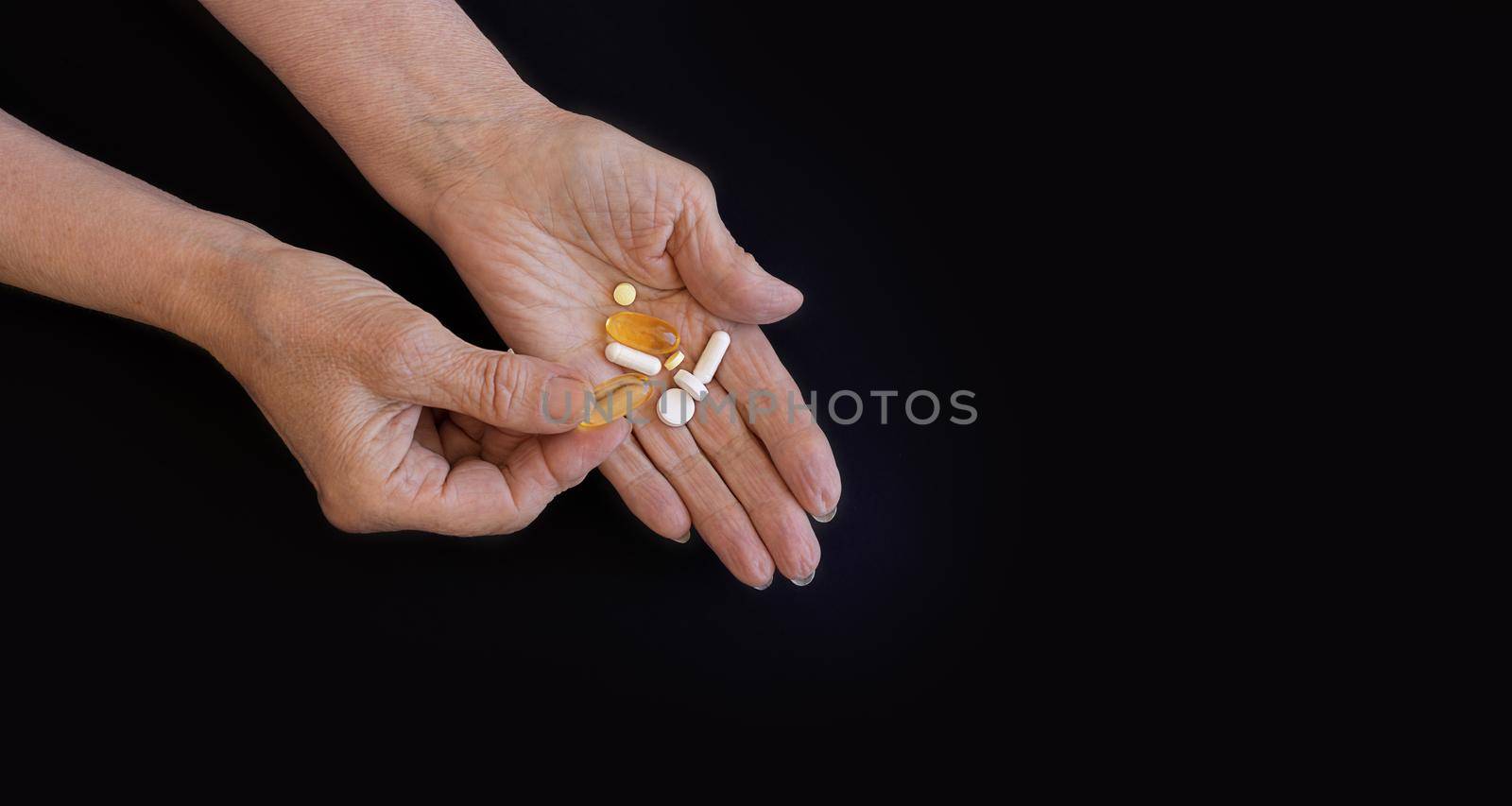 An elderly woman chooses which pill to take, hands on a black background by Ramanouskaya
