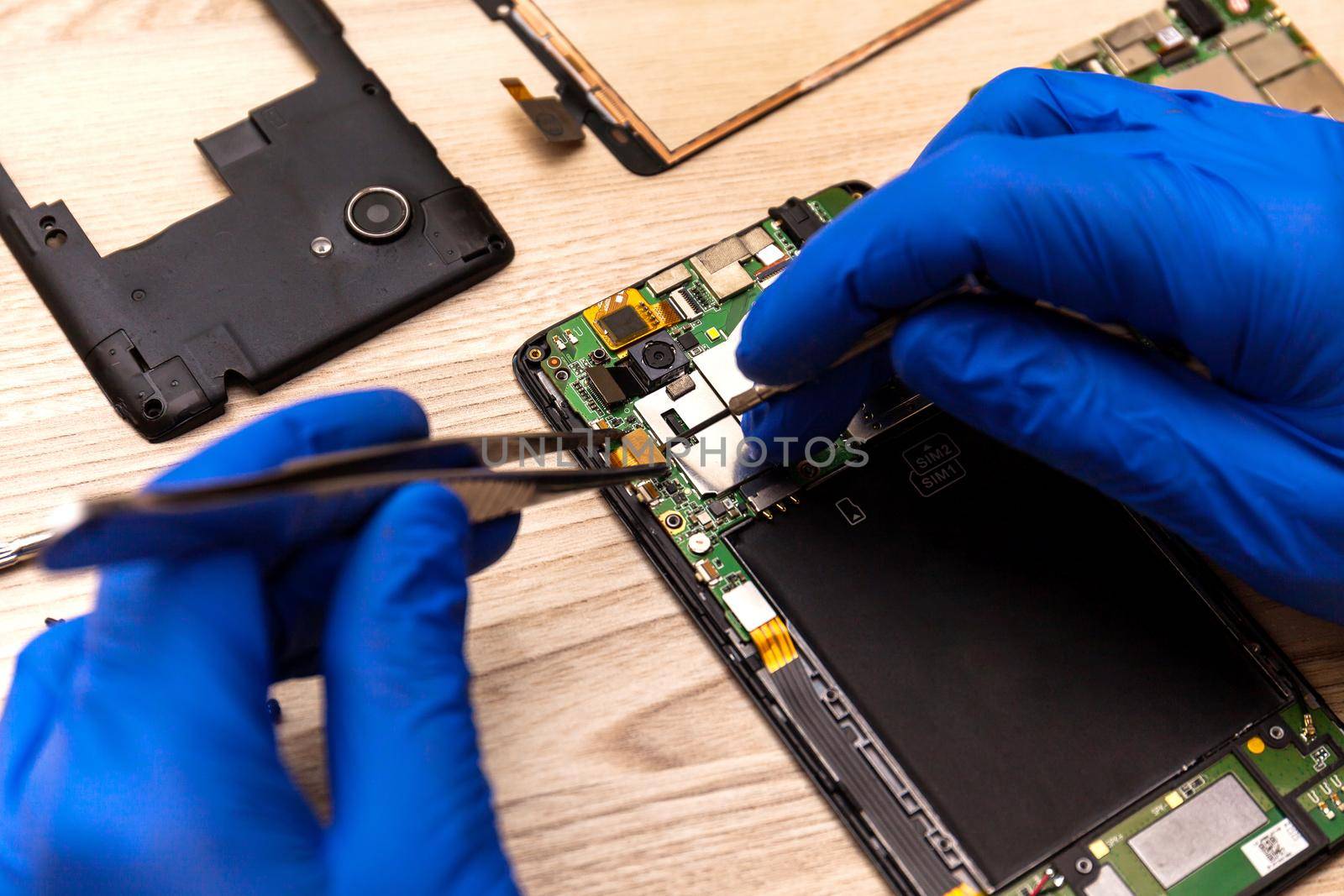The technician repairing the smartphone's motherboard in the workshop on the table. by InnaVlasova