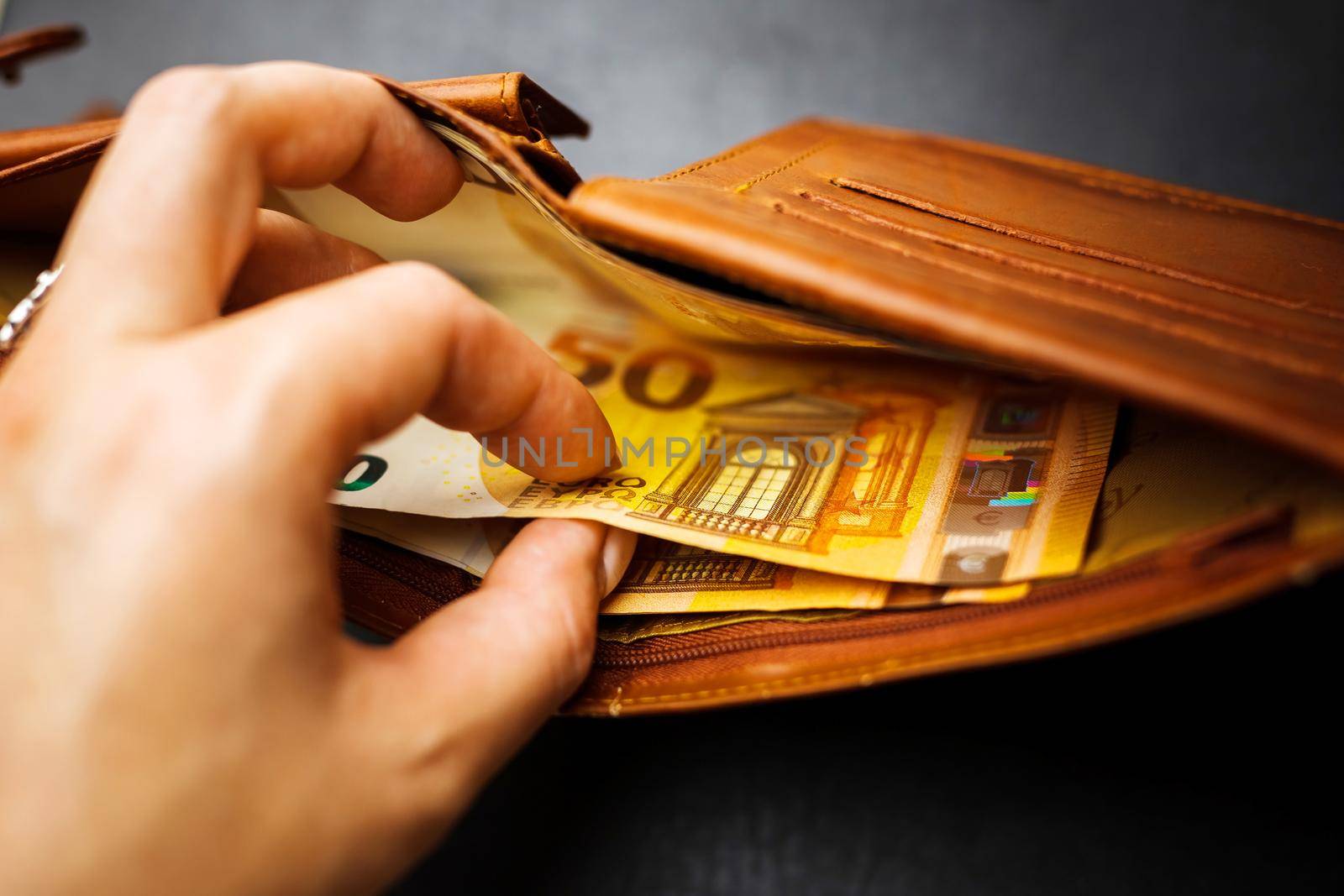 Woman's hand hand takes out banknotes from a brown wallet with euro money. Soft focus
