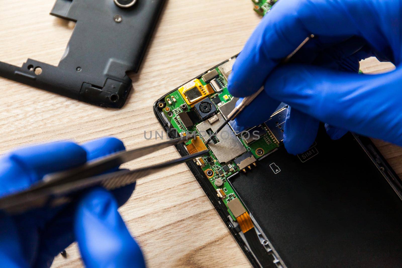 The technician repairing the smartphone's motherboard in the workshop on the table. by InnaVlasova