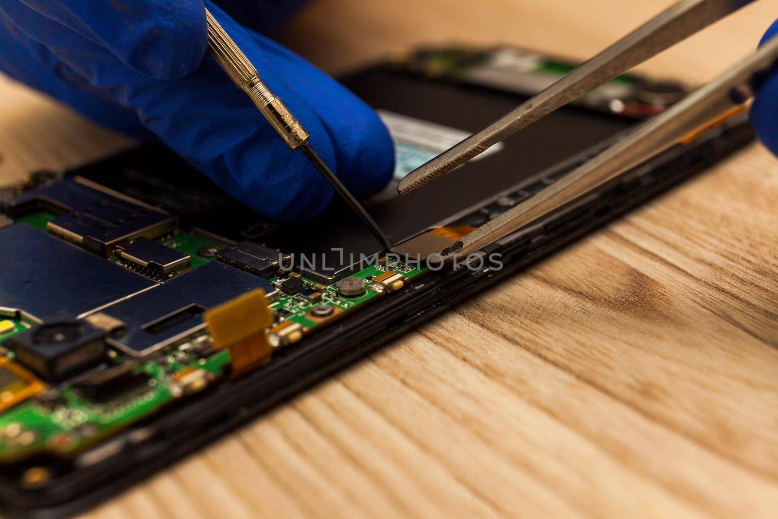 The technician repairing the smartphone's motherboard in the workshop on the table. by InnaVlasova