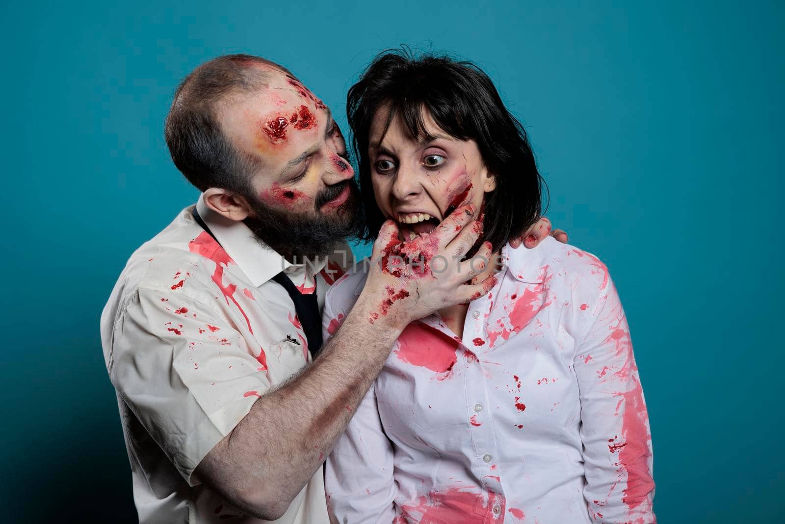 Undead zombies biting hand on camera, acting aggressive and dangerous in studio. Crazy evil monsters showing teeth and having bloody wounds, looking creepy and deadly with scars and scratches.