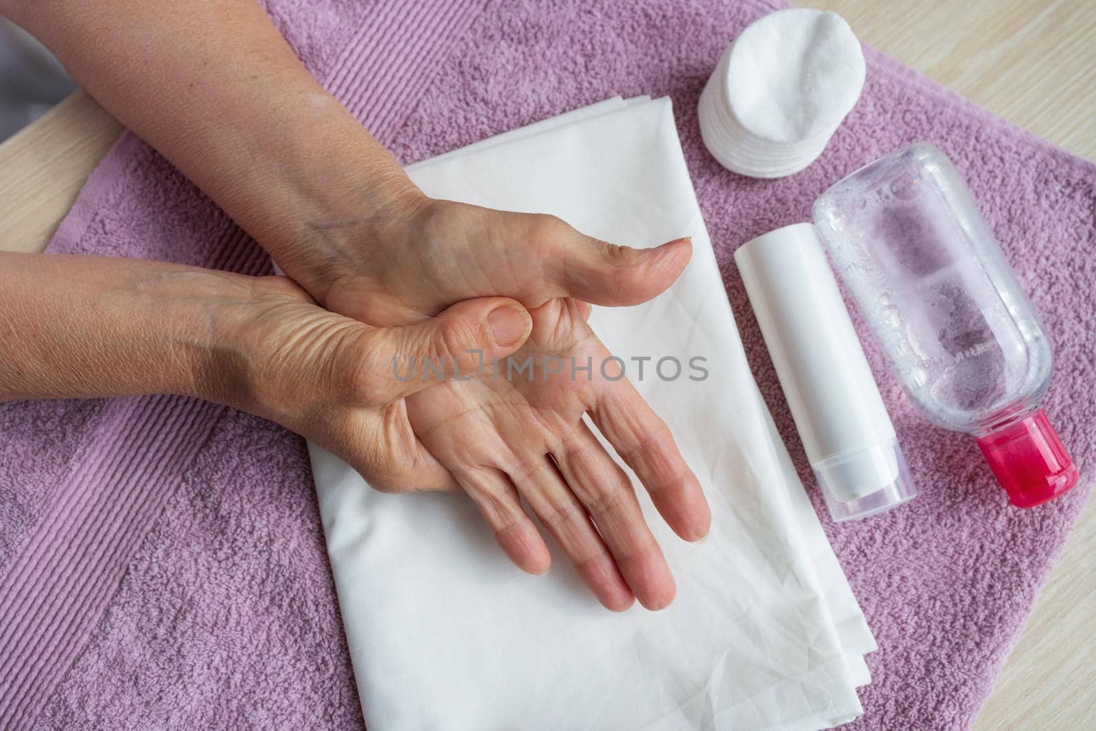 close-up of the hands of an elderly woman with arthritis and wrinkles give herself a hand massage. Nearby are hand cream and tonic. cream bottle mockup. Prevention of neurological diseases in the elderly, self-care.