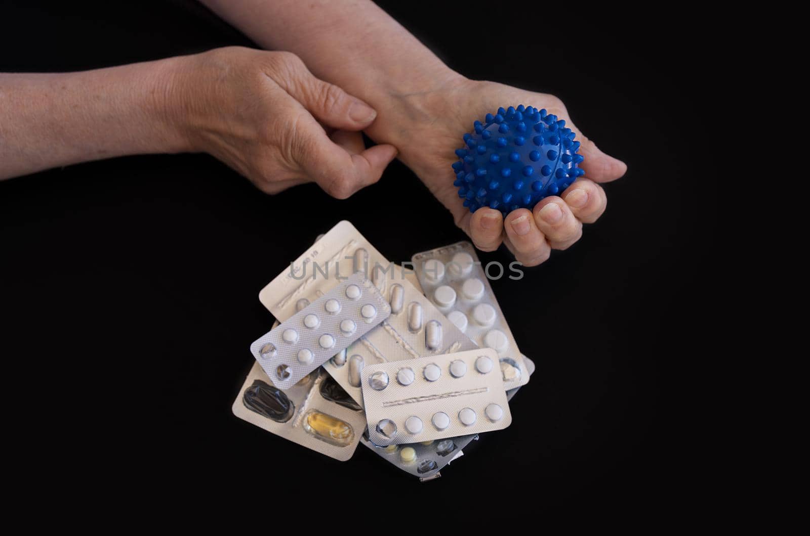 close-up, the hands of elderly woman perform self-massage exercises with prickly blue ball against the background of handful of pills. The concept of alternative medicine, the prevention of diseases