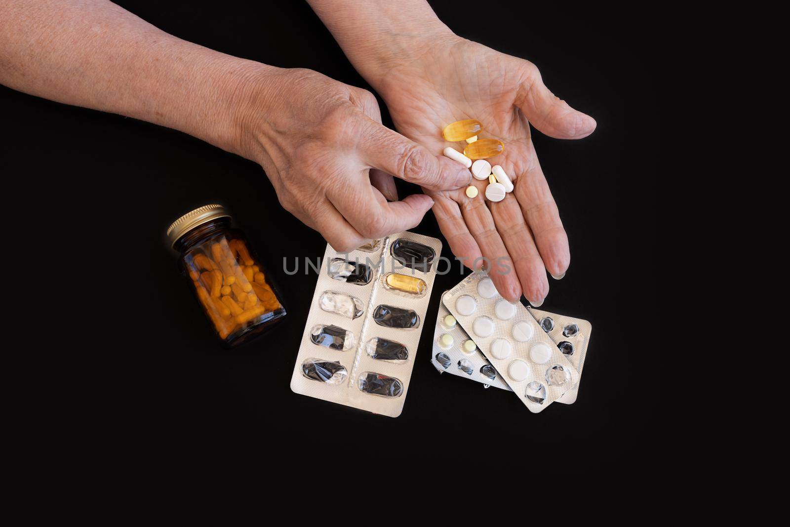 Close-up, a large number of different pills on a black background in the hands of an elderly woman by Ramanouskaya