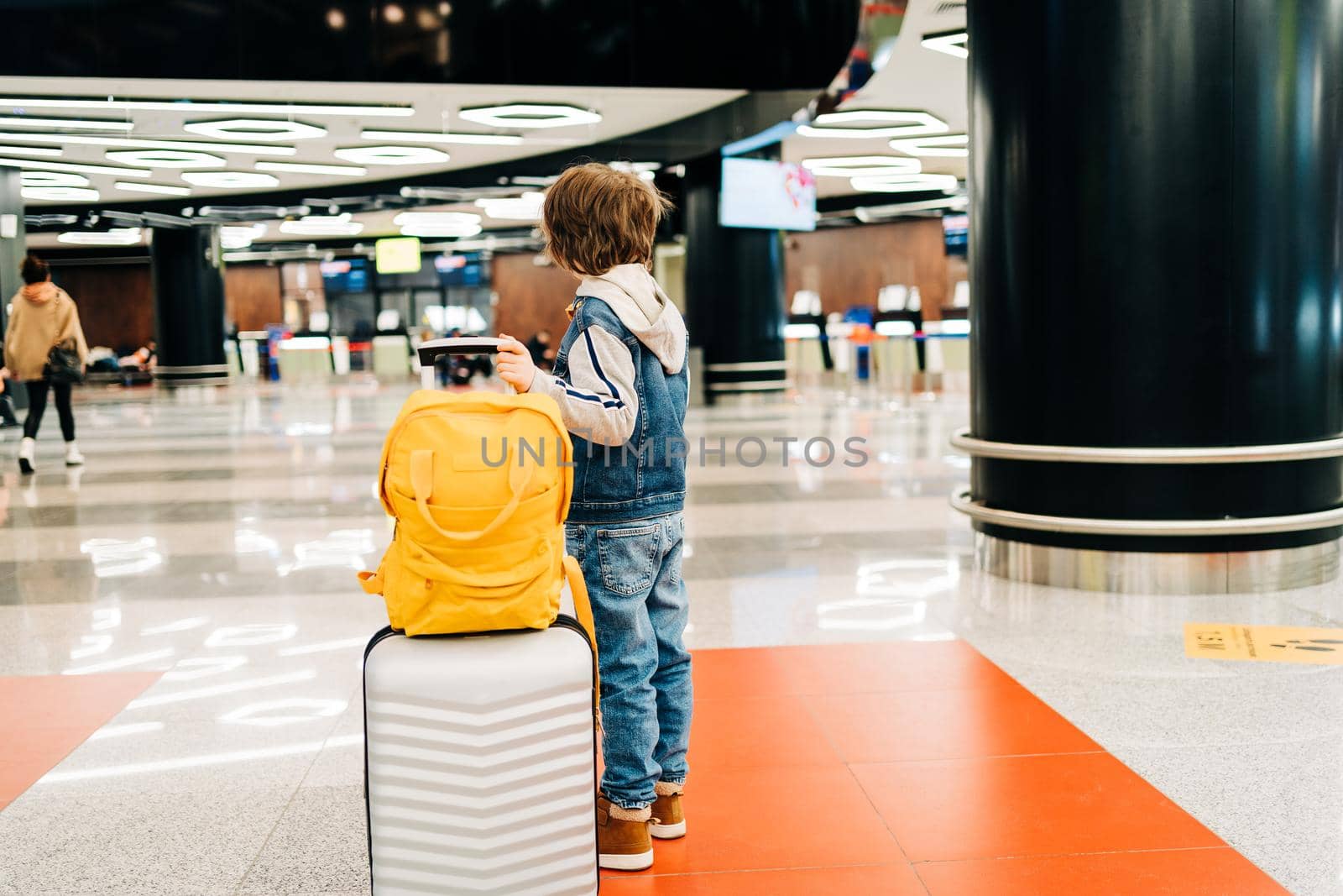 Child boy with backpack standing in the airport terminal, waiting for flight, travel with suitcase. Vacation concept by Ostanina