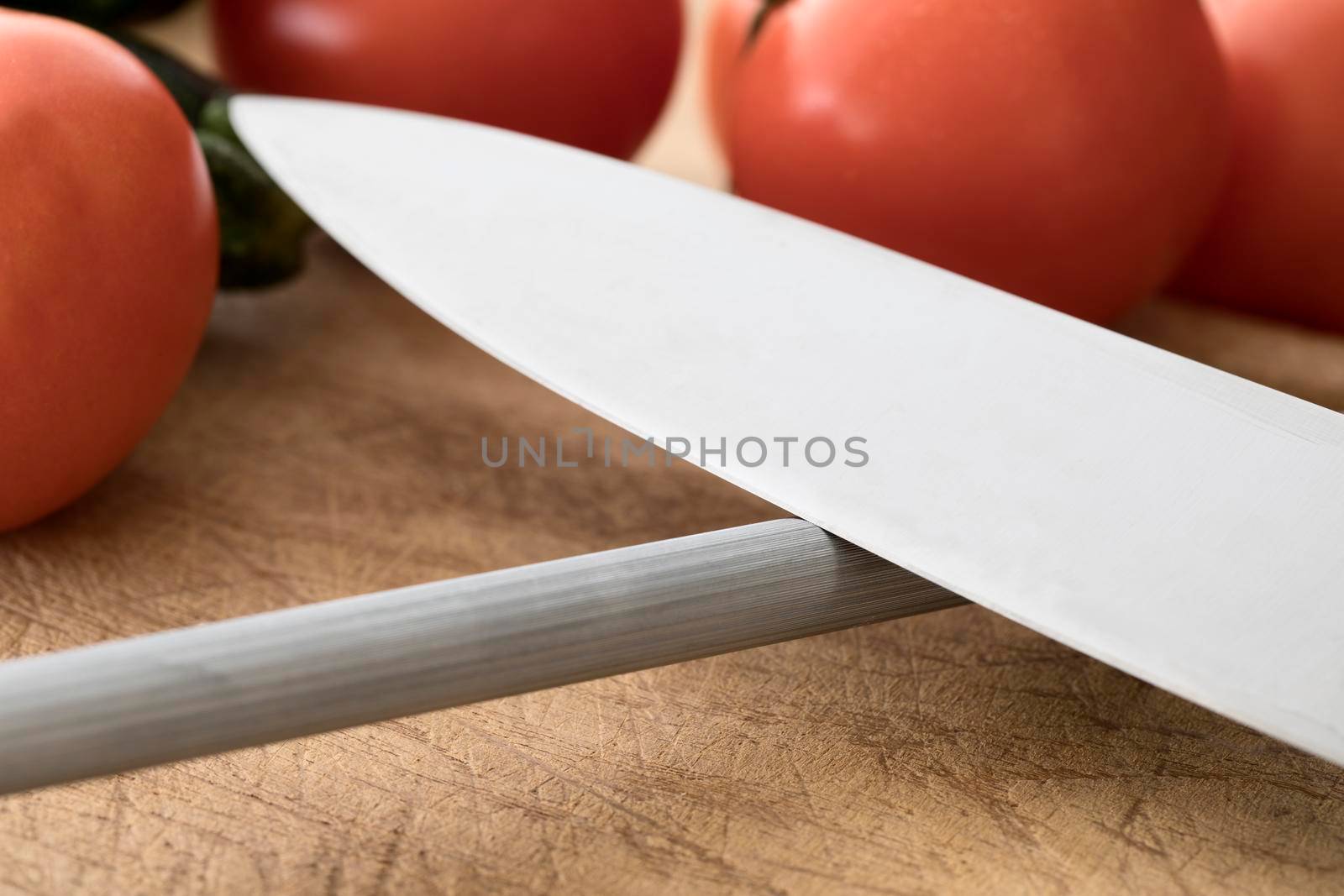 Close up of knife on honing steel with vegetables in background