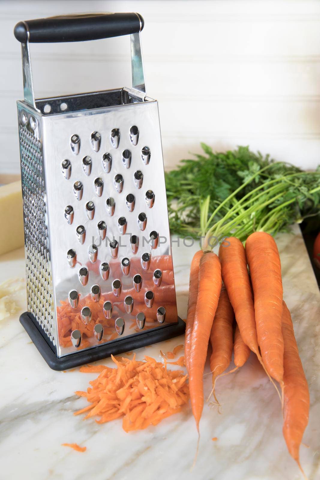 Cheese grater with whole and grated carrots on marble surface.