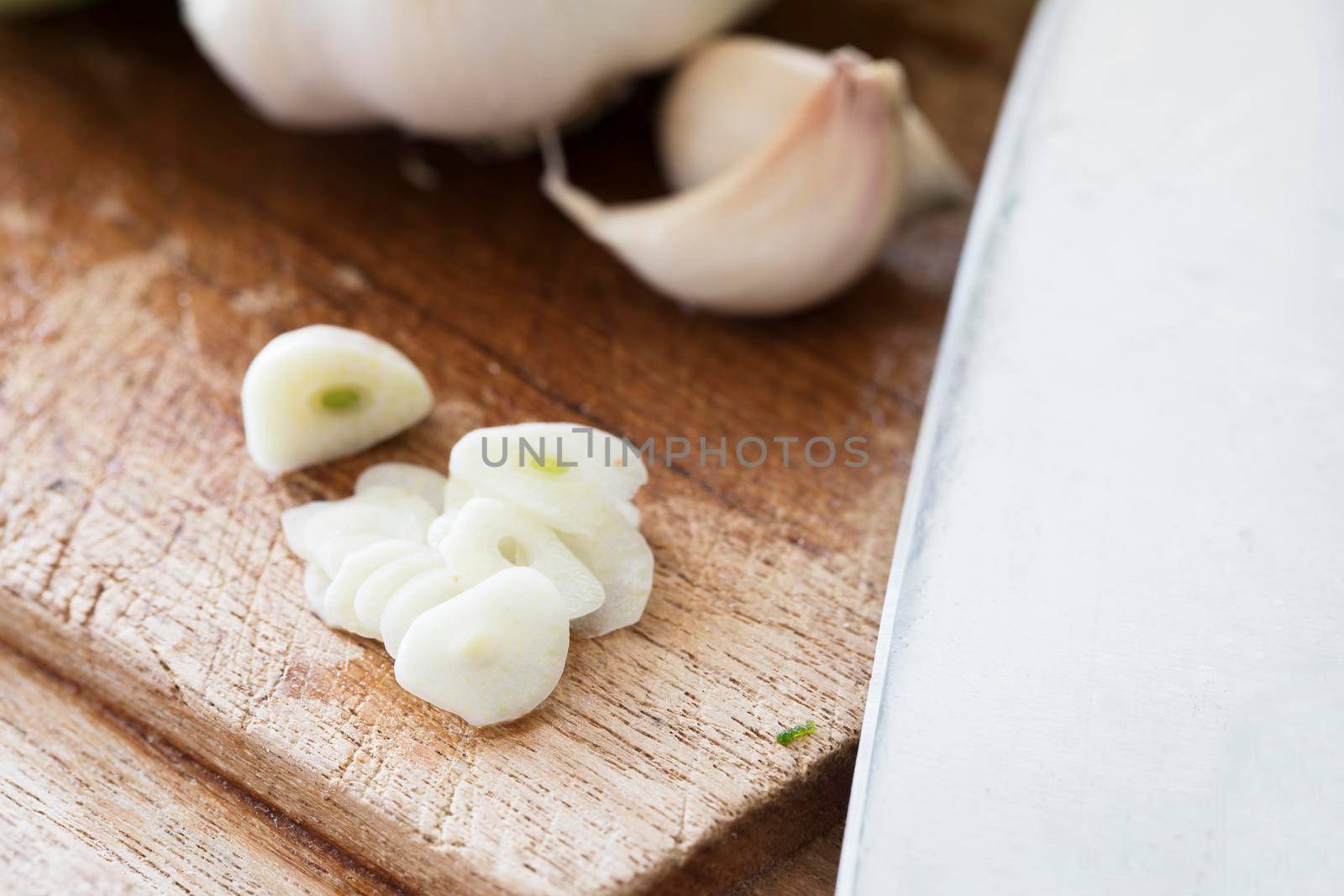 Close up of garlic slices on cutting board with knife