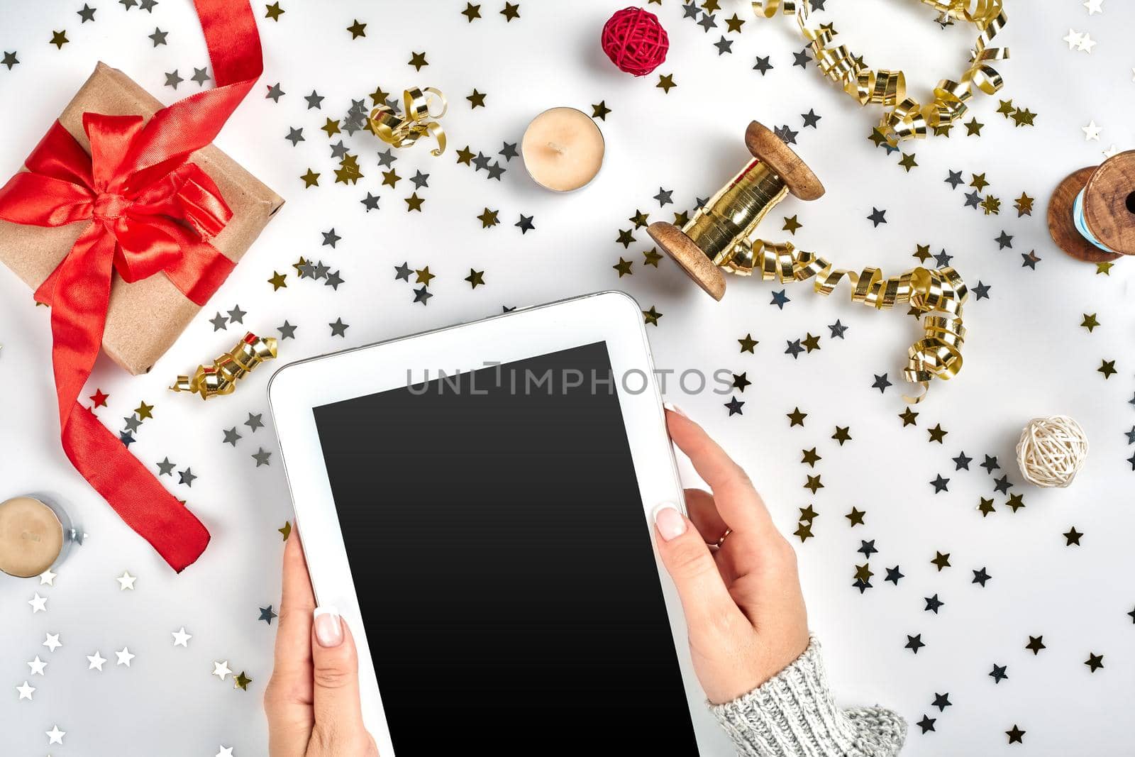 Flat lay, Top view Christmas composition on white background. Digital tablet, gift box with red fabric tape, spiral ribbon, gold beads, stars confetti. Xmas concept