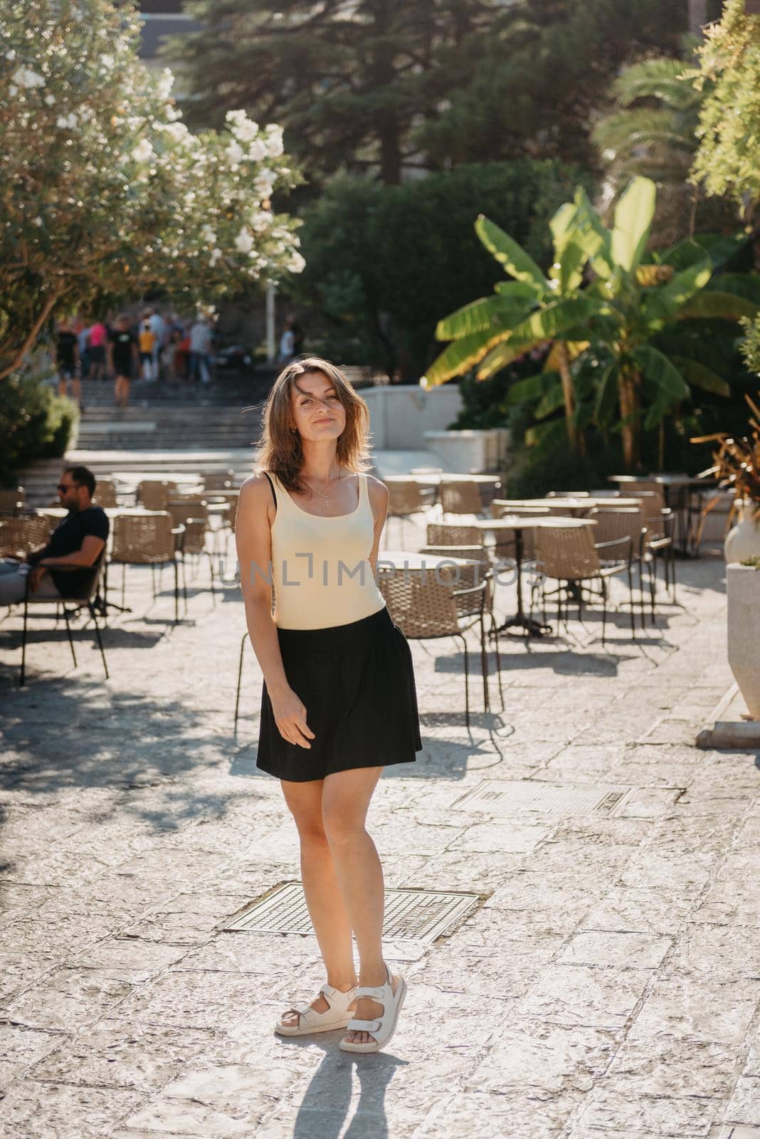 Girl tourist walking through ancient narrow street on a beautiful summer day in MEDITERRANEAN MEDIEVAL CITY , OLD TOWN bUDVA, MONTENEGRO. Young beautiful cheerful woman walking on old street at tropical town. Pretty girl looking at you and smiling