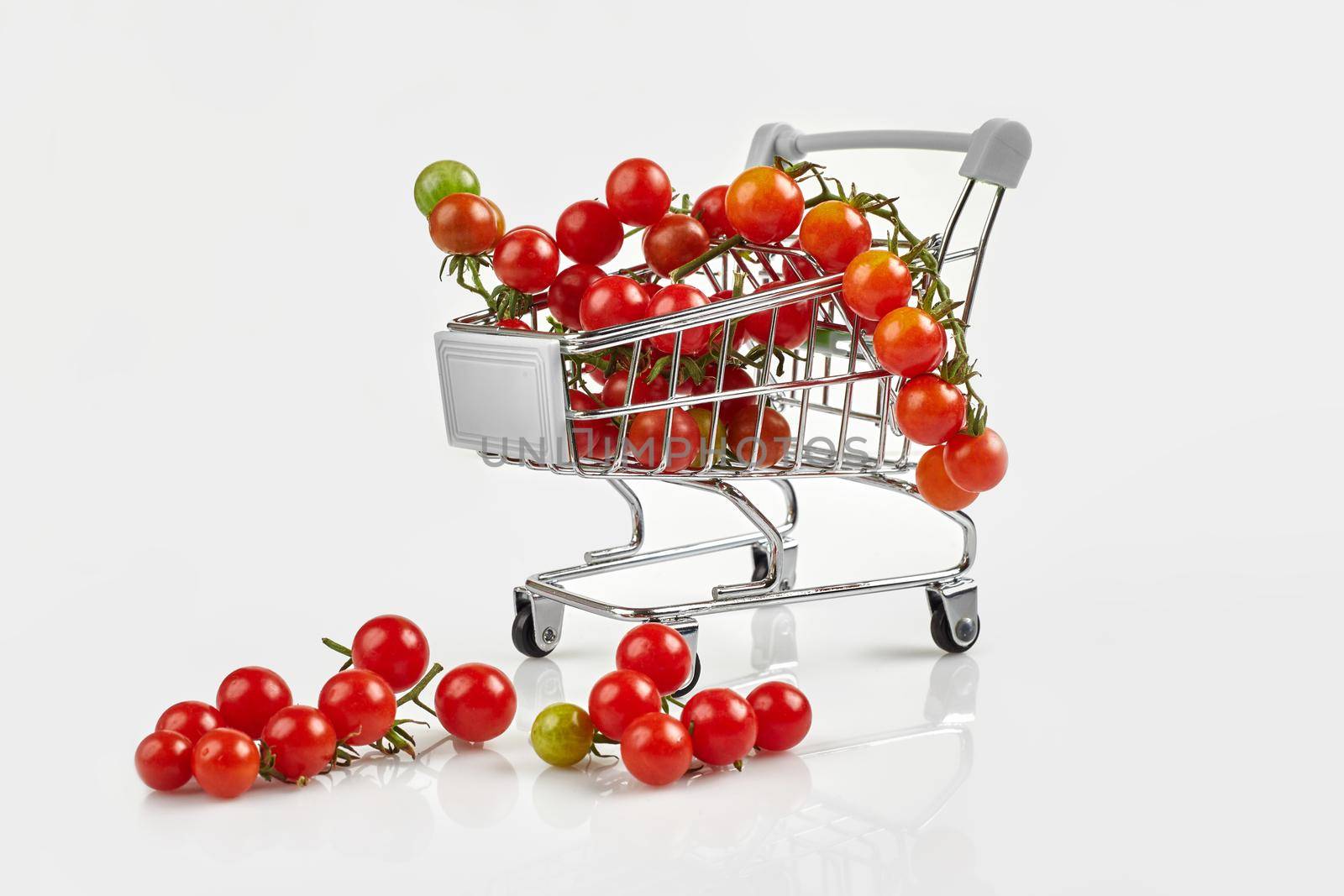 Mini shopping cart full with cherry tomatos on white background. Copy space