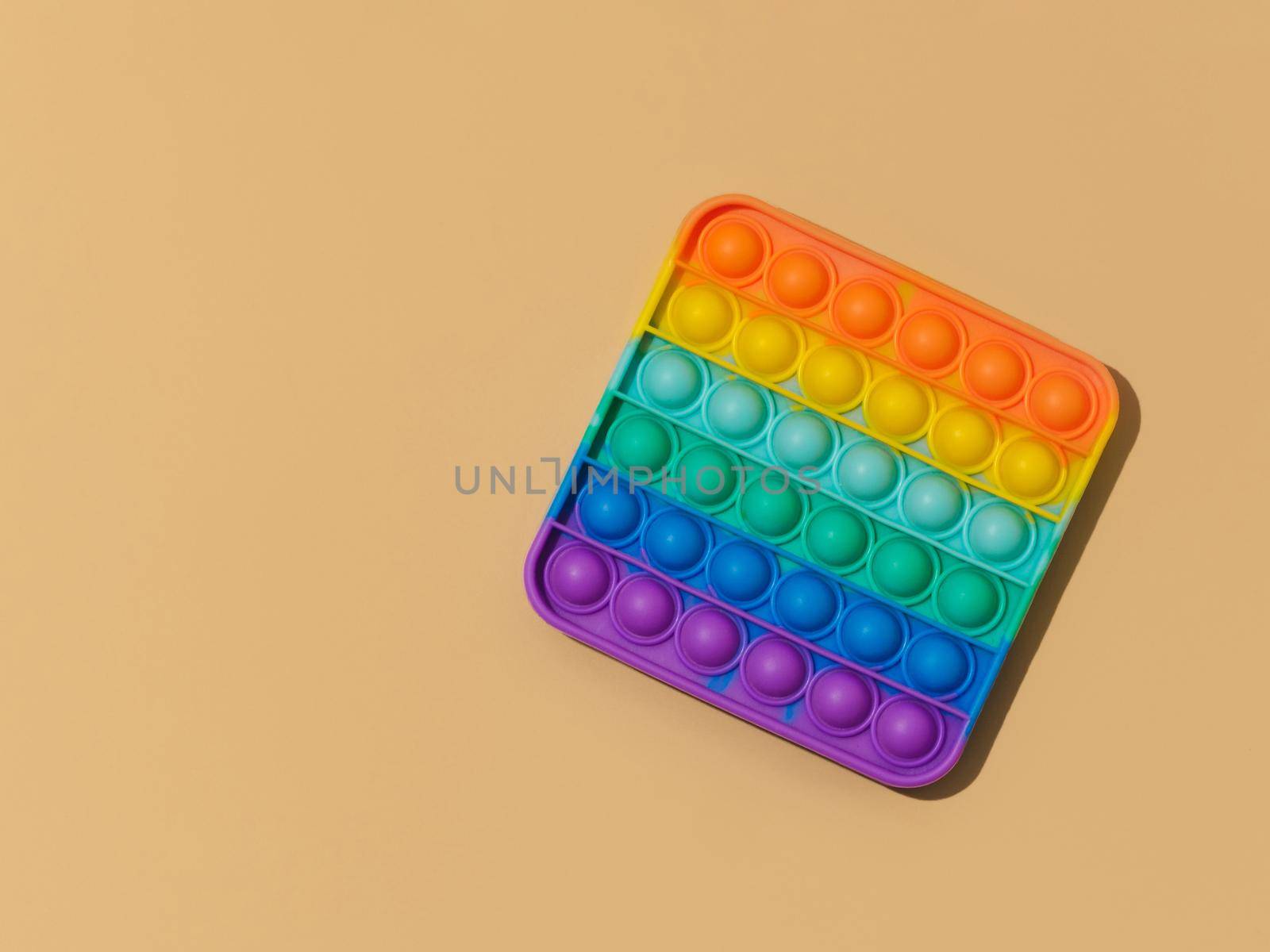 Popit on pastel beige background with copy space. Popular silicone colorful antistress pop it toy for child. Top view. Simple dimple. Bright light with hard shadows