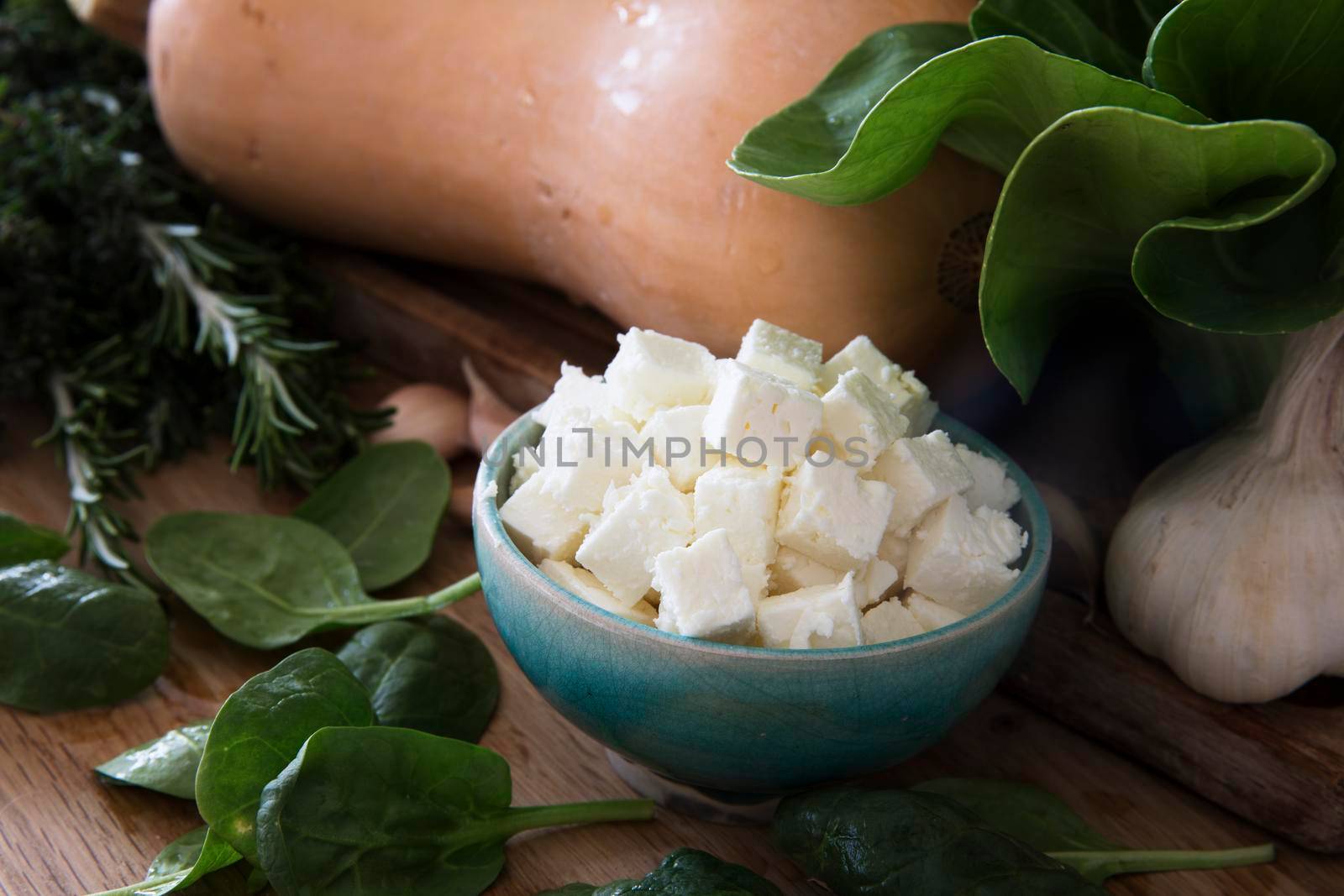 Bowl of feta cheese surrounded by spinach, garlic and a butternut squash.