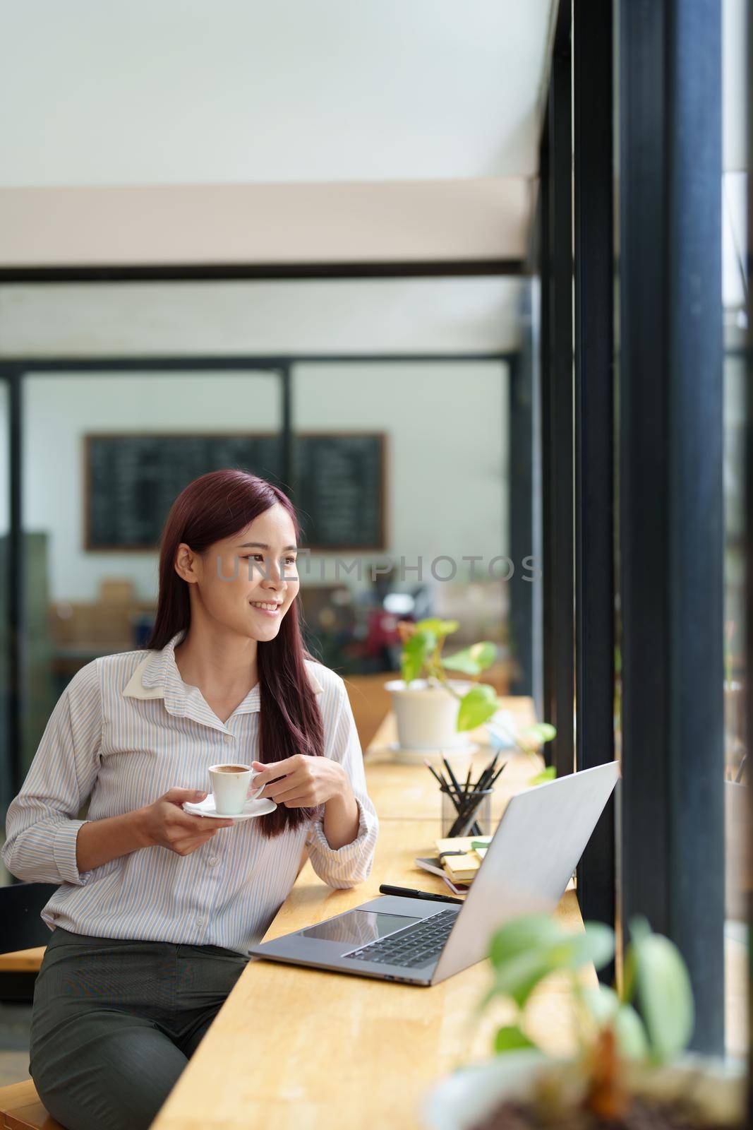 Asian business woman drinking coffee and using computer in office.