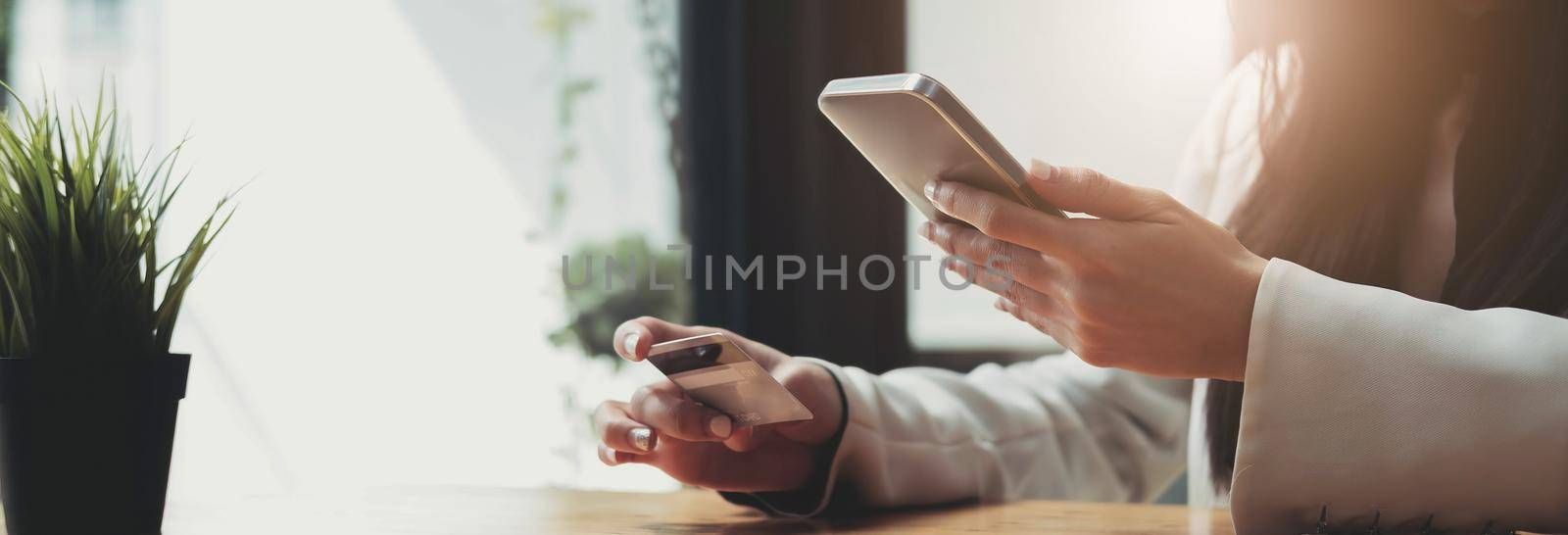 Hands holding credit card and using mobile smart phone at cafe. by wichayada