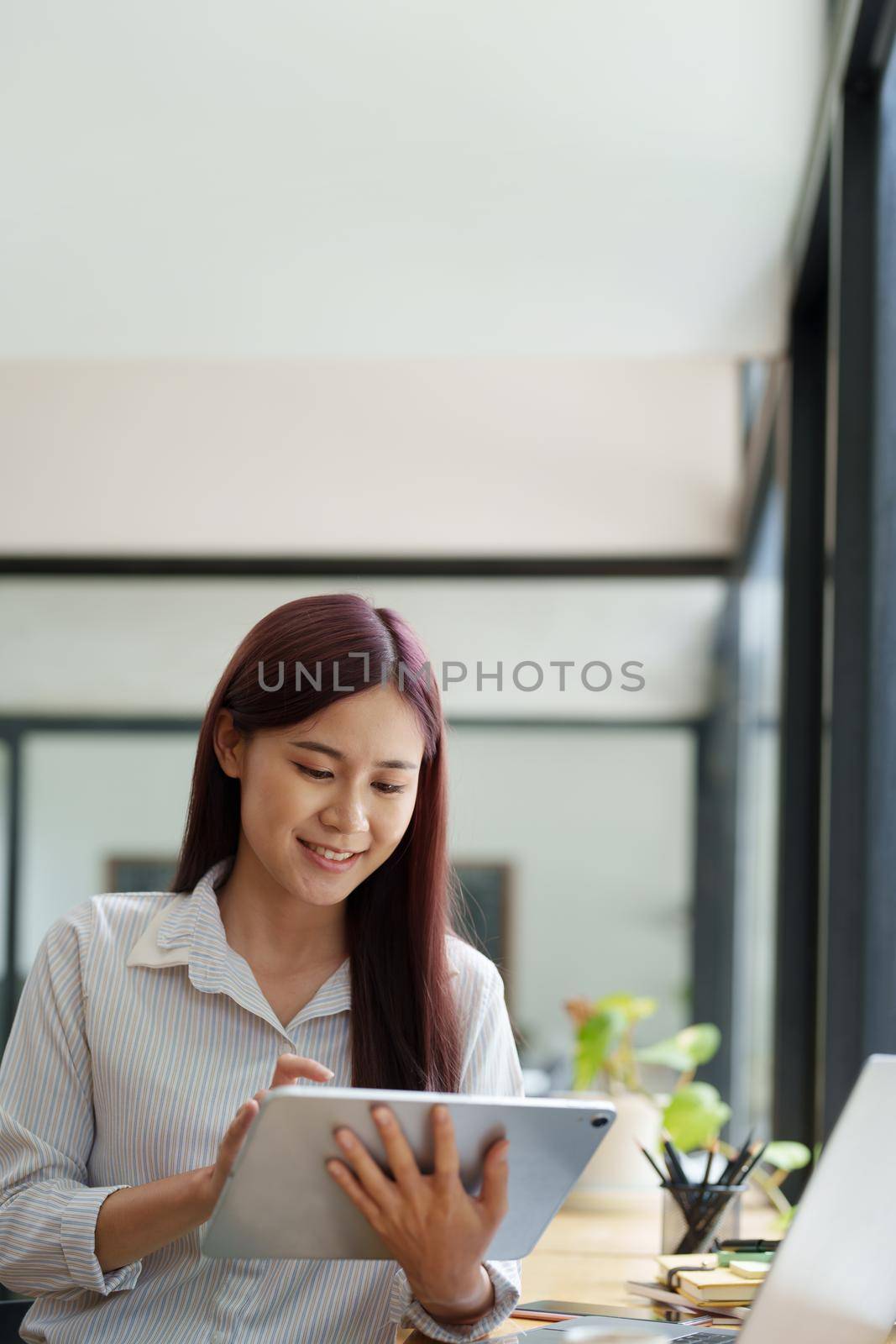 Portrait of an Asian female employee using a tablet computer at work. by Manastrong
