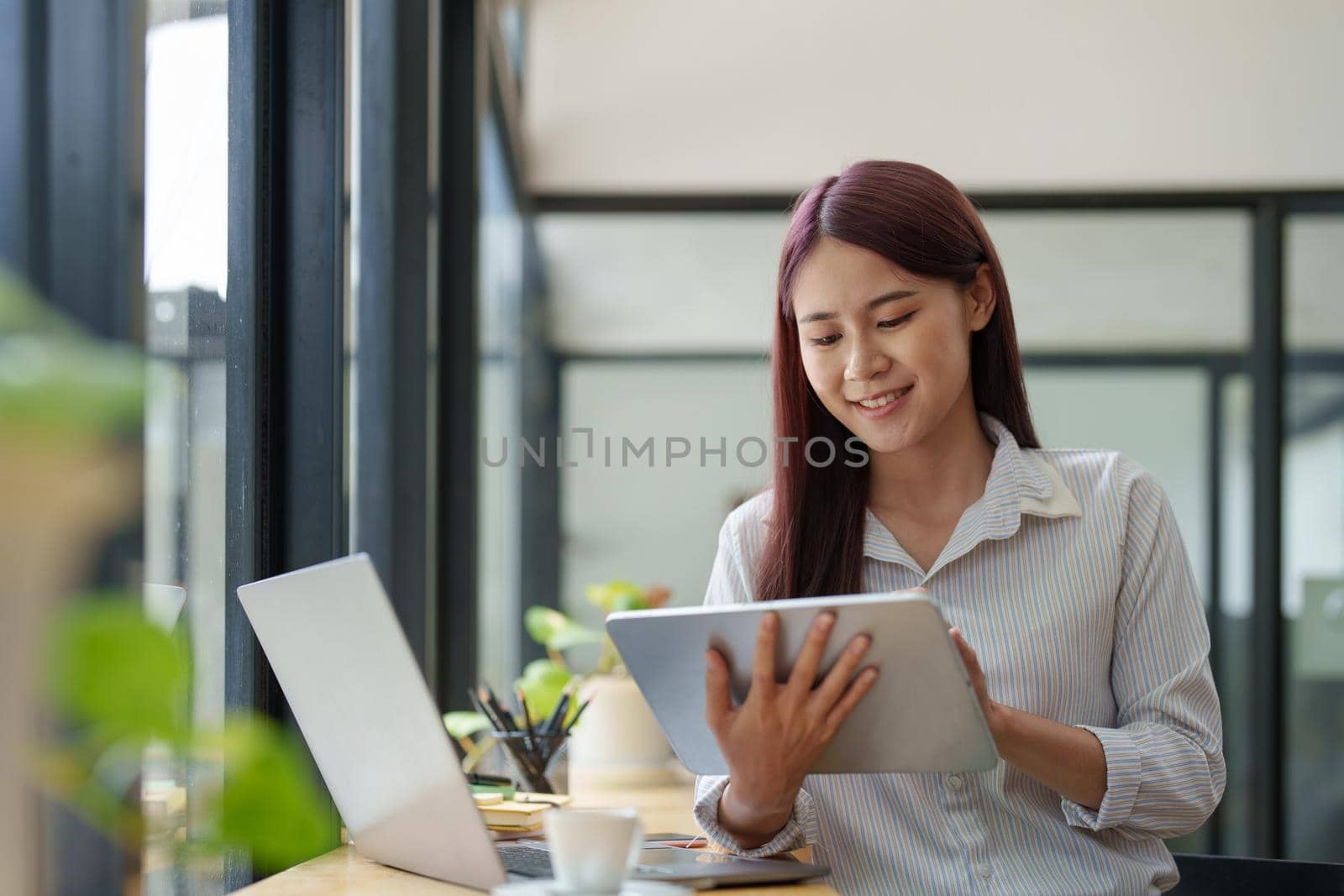 Portrait of an Asian female employee using a tablet computer to work to gather information and analyze marketing plans and investment budgets to increase company profits.