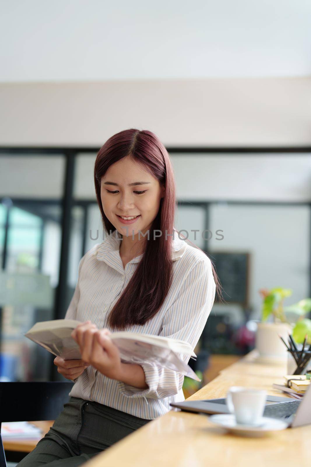 Portrait of an Asian woman reading a book during her lunch break by Manastrong