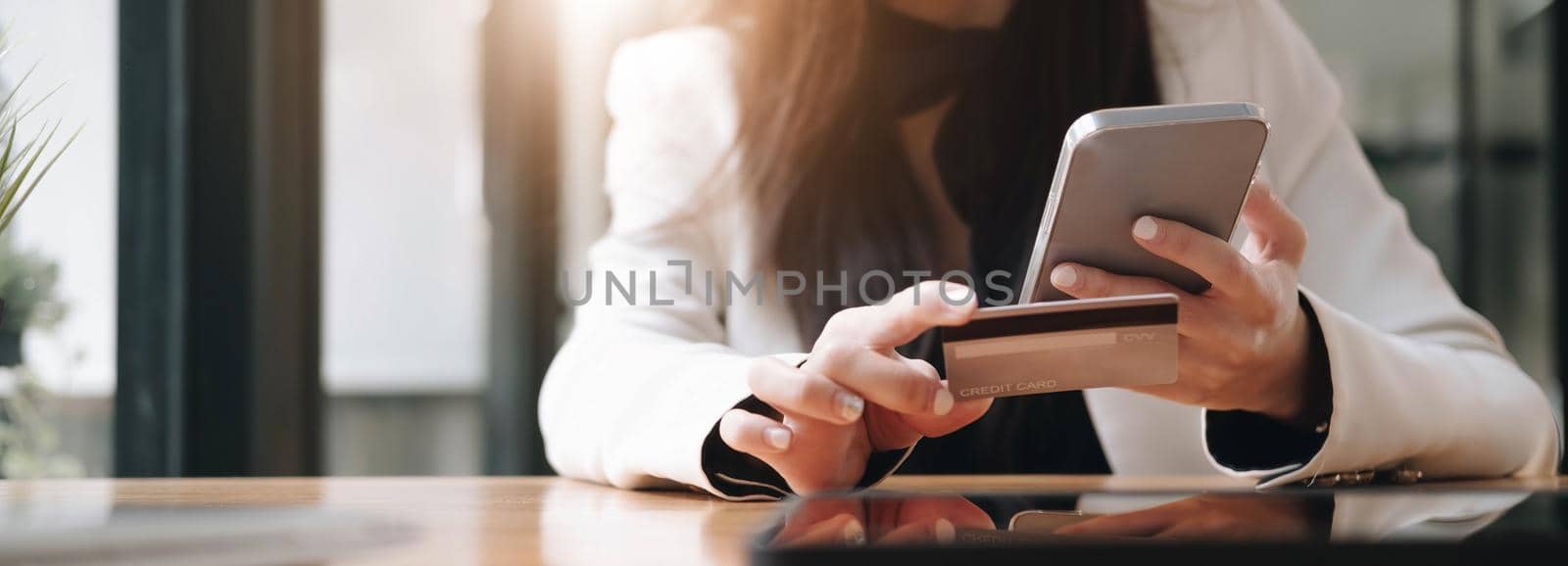 Close up female hands holding credit card and smartphone, young woman paying online, using banking service, entering information, shopping, ordering in internet store, doing secure payment by wichayada