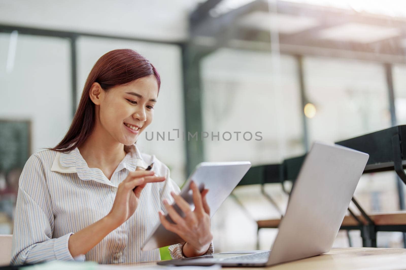 Portrait of an Asian female employee using a tablet computer to work to gather information and analyze marketing plans and investment budgets to increase company profits.