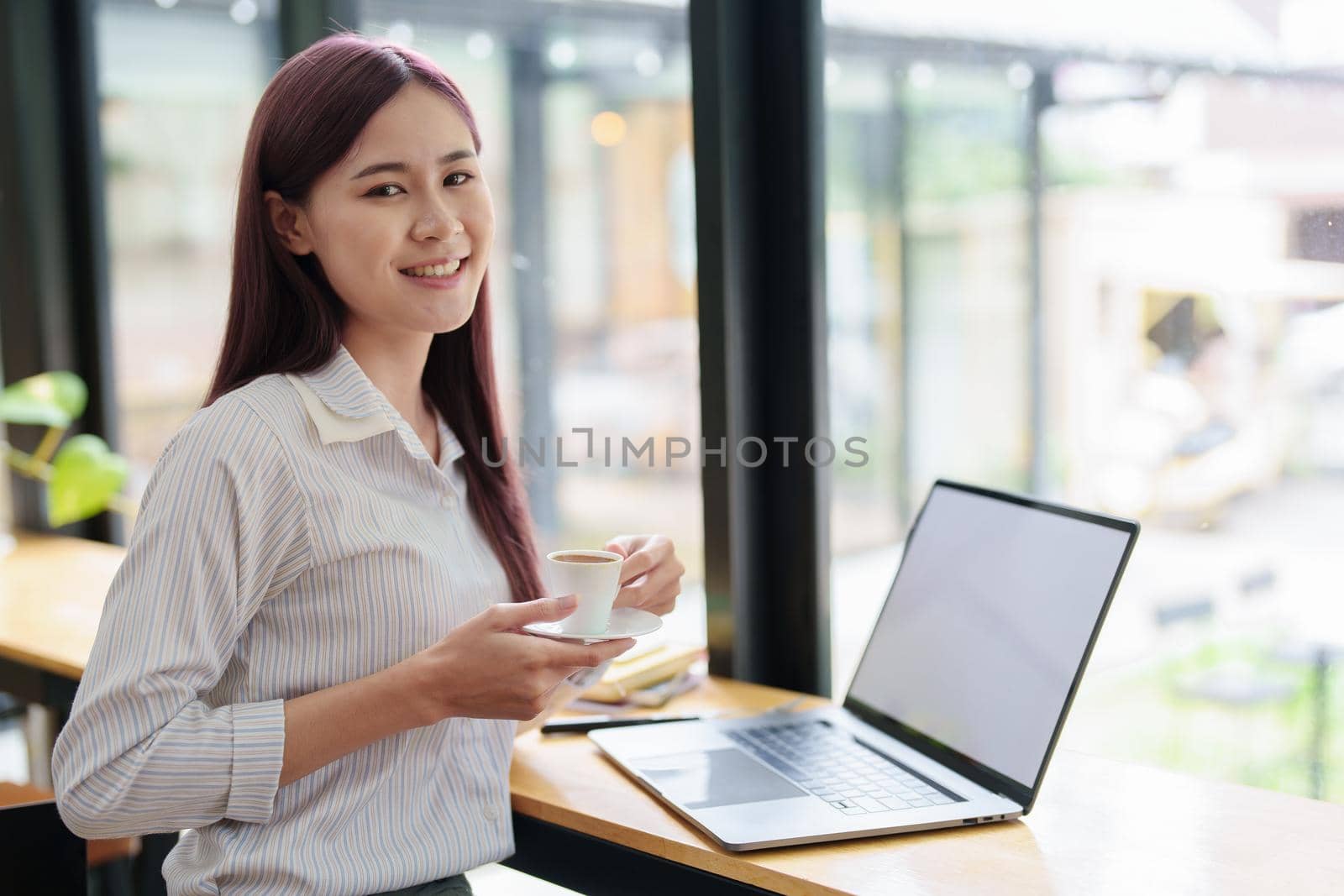 Asian business woman drinking coffee and using computer in office by Manastrong