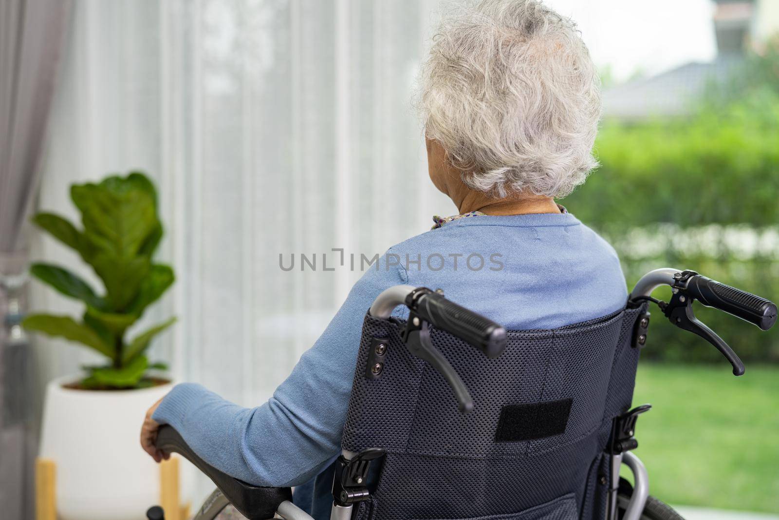 An elderly woman sitting on wheelchair looking out the window for waiting someone. Sadly, melancholy and depressed.