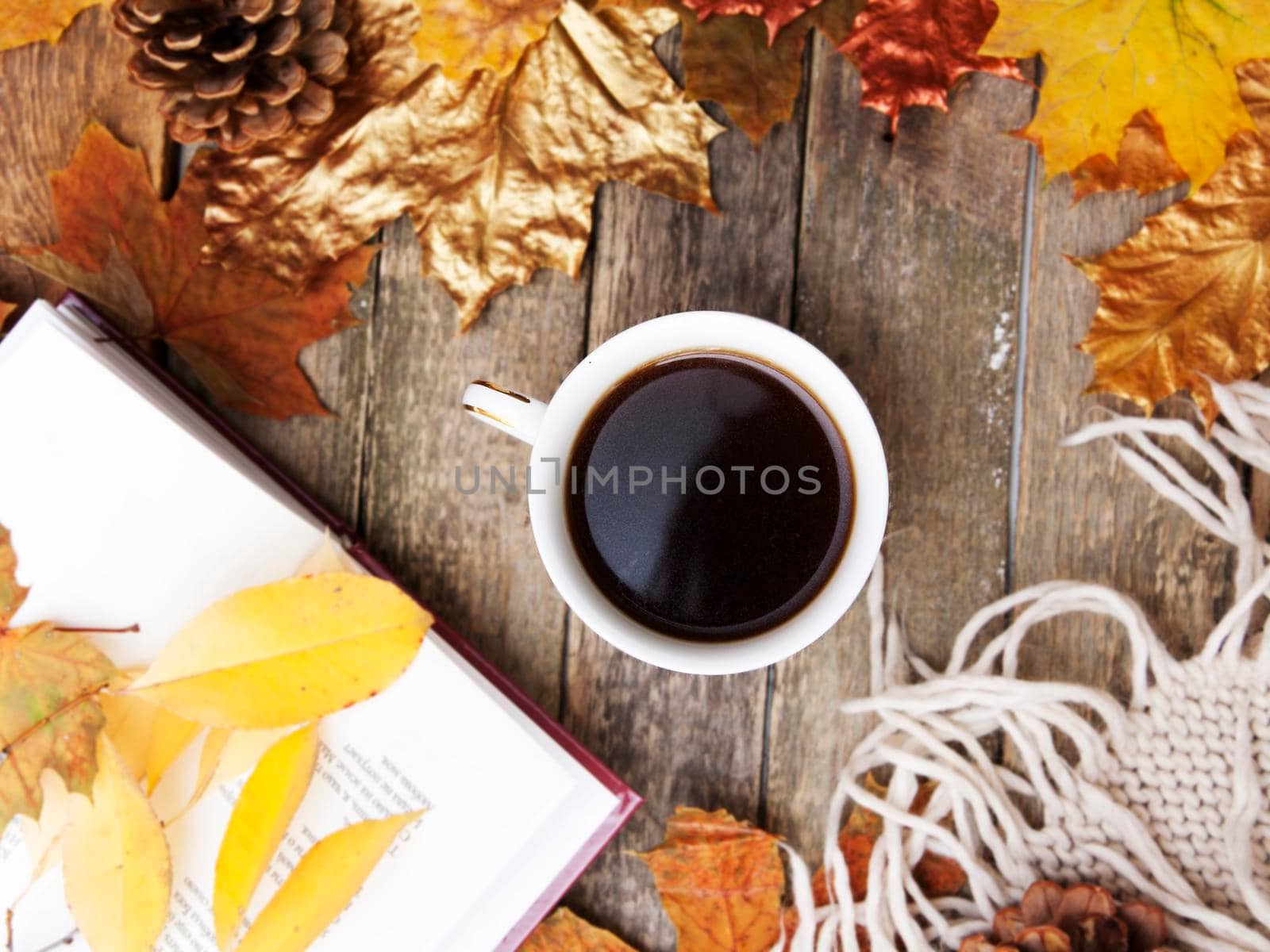 Autumn layout: hot coffee, book, golden autumn leaves, knitted sweater, plaid on a wooden table. Cozy autumn mood in October, November
