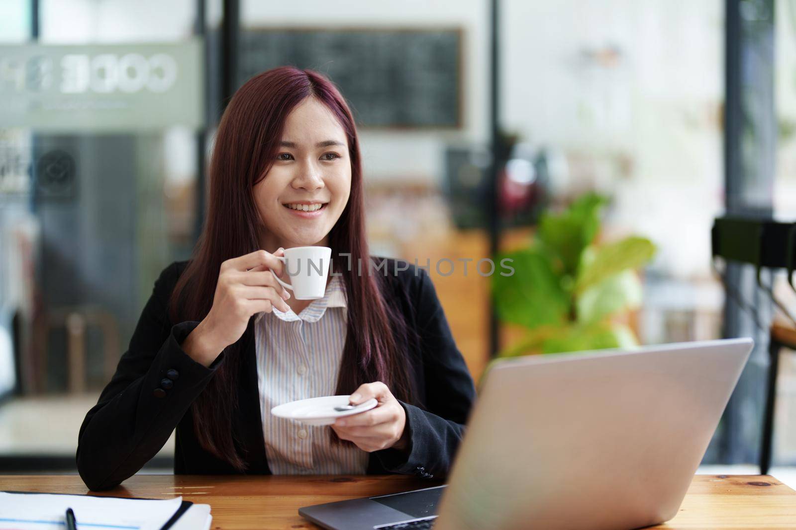 Asian business woman drinking coffee and using computer in office by Manastrong