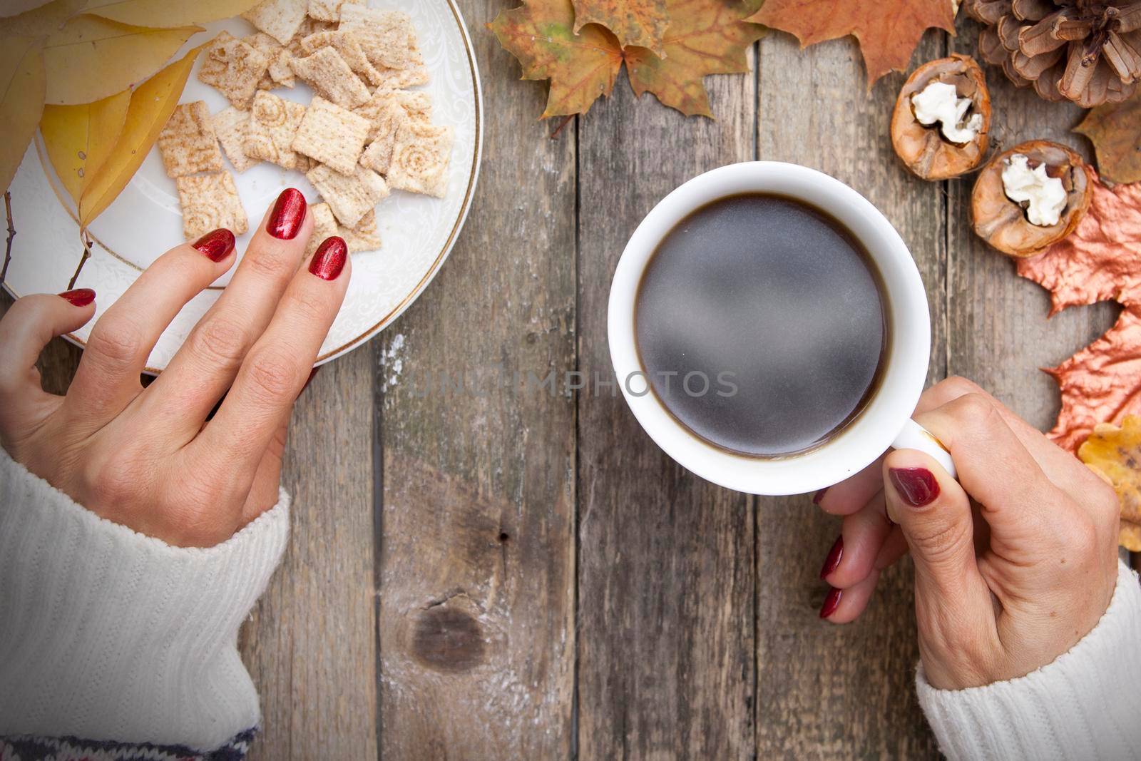 Hot coffee in the hand of a wooman, autumn leaves, a knitted warm sweater, cookies. Cozy autumn mood in October, November