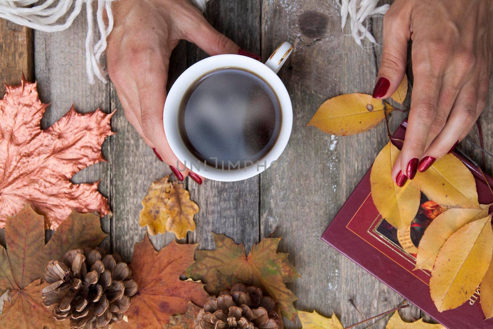 Top view cup of coffee in female hands on a wooden table background with autumn leaves, cones. Top view