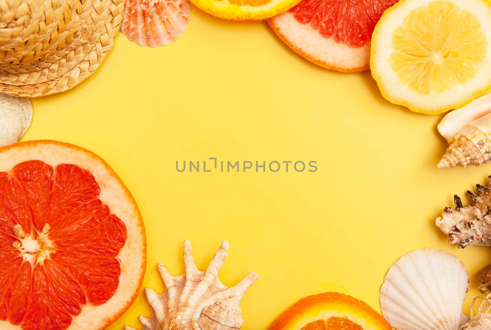 Flat lay slices of orange, grapefruit and lemon with shells on a yellow background. Summer citrus pattern with copy space by ssvimaliss