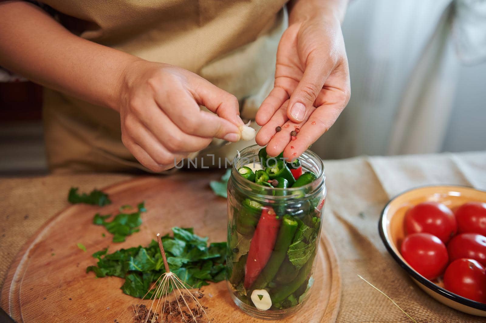 Top view of a woman putting peppercorns into a canning jar with pickled chili peppers, making pickles at home kitchen. Pickling. Preservation of seasonal organic vegetables. Family traditional recipe