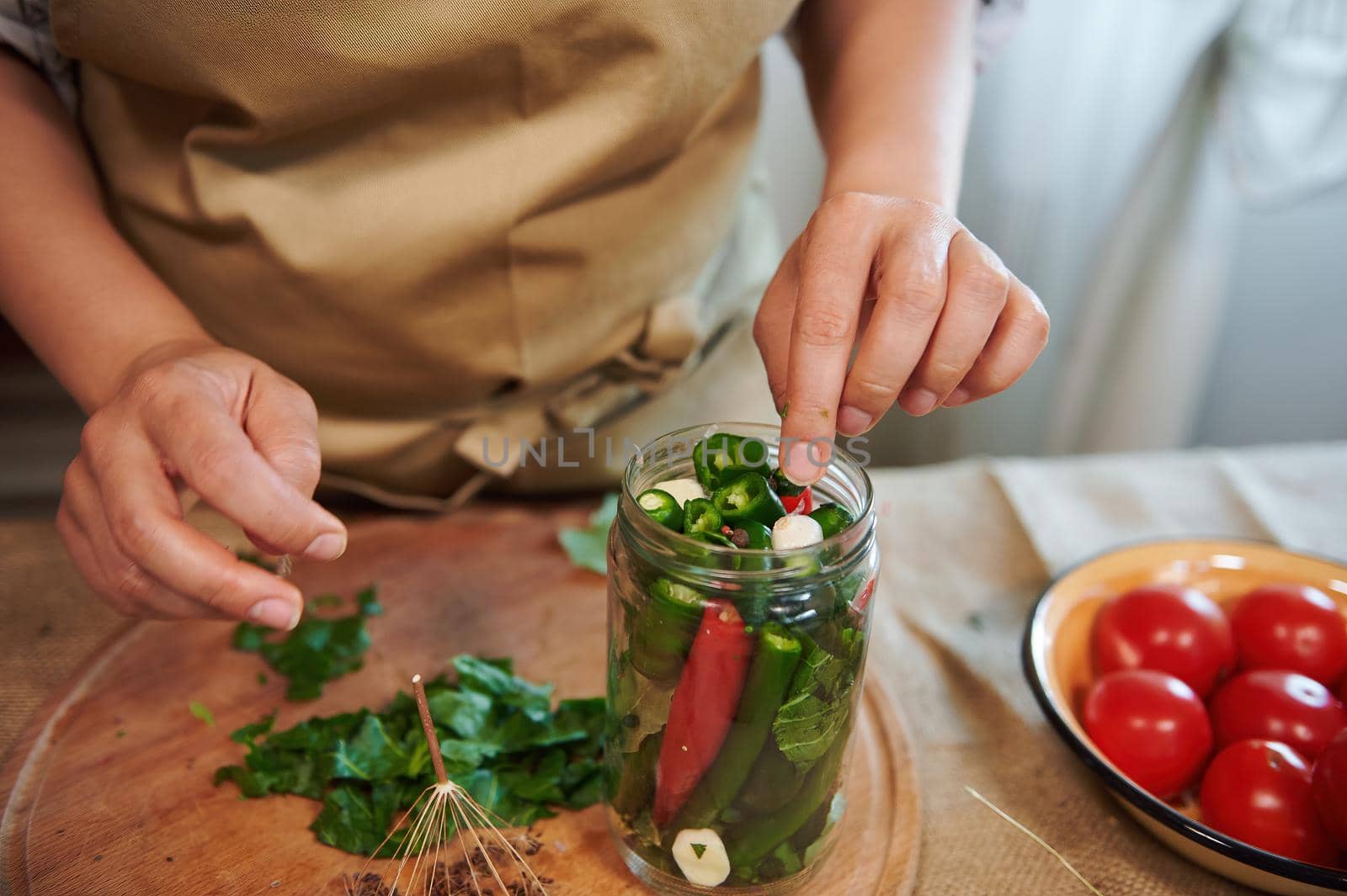 Cropped view of housewife's hand adding fragrant culinary herbs in freshly marinated chili peppers. Close-up pickling by artgf