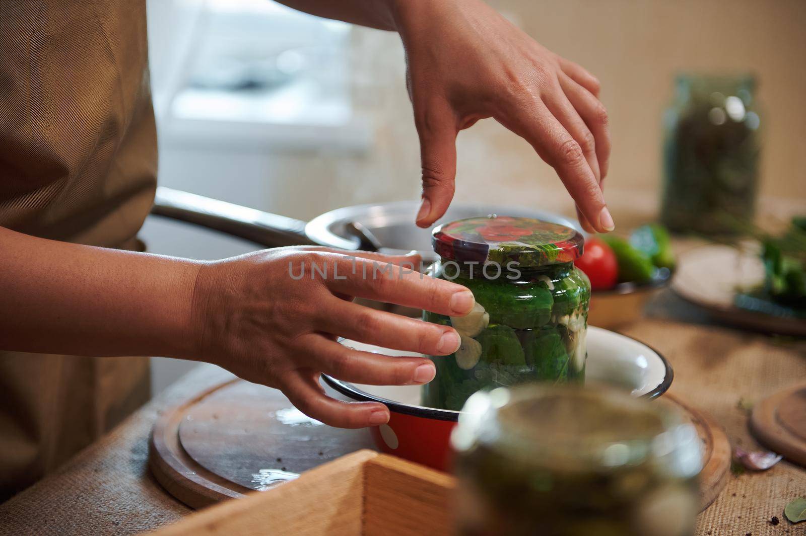 Details: housewife's hands cover with a sterilized lid a glass jar with freshly pickled organic cucumbers. Canning, marinating, pickling concept. Preparing homemade marinated delicacies for the winter